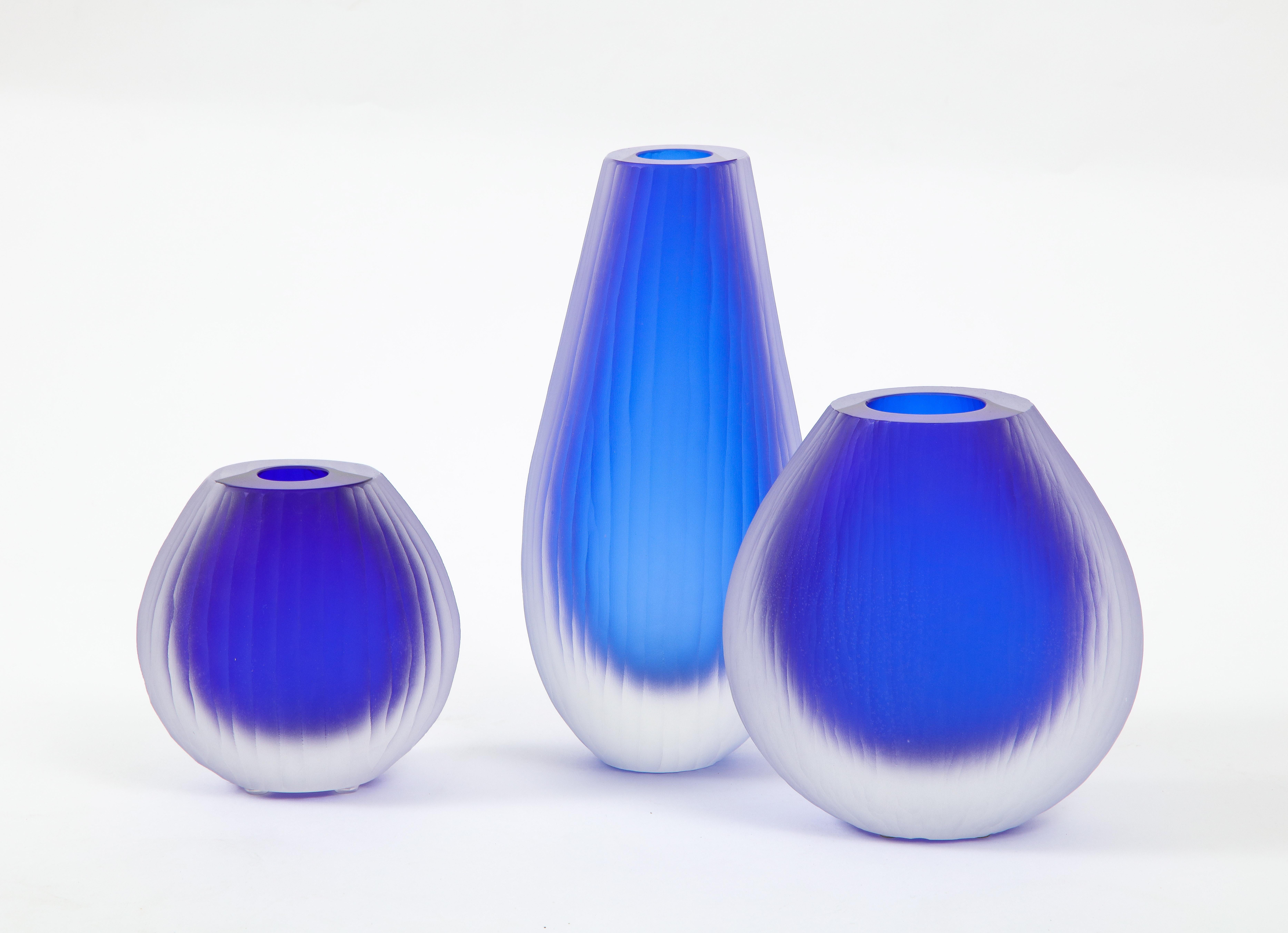 Un set di tre vasi in vetro di Murano scanalato blu cobalto e trasparente di dimensioni diverse, opera del maestro veneziano Alberto Donà. Il vaso più alto misura 12