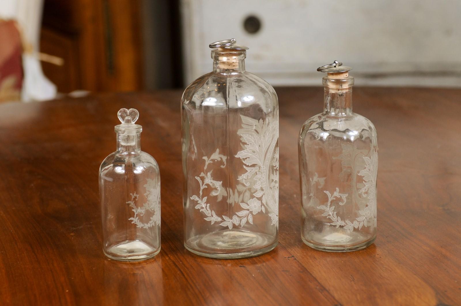 A set of three glass vanity bottles from the 19th century, with etched floral décor. Created in France during the 19th century, each of this set of three vanity bottles features an oblong body adorned with etched floral motifs. Oval medallions
