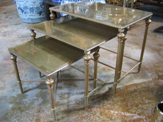 Neoclassically detailed nesting tables with gold-leafed mirrored tops. Antiqued finish with some distressing due to age. Bronze frames and legs have an antiqued patina.