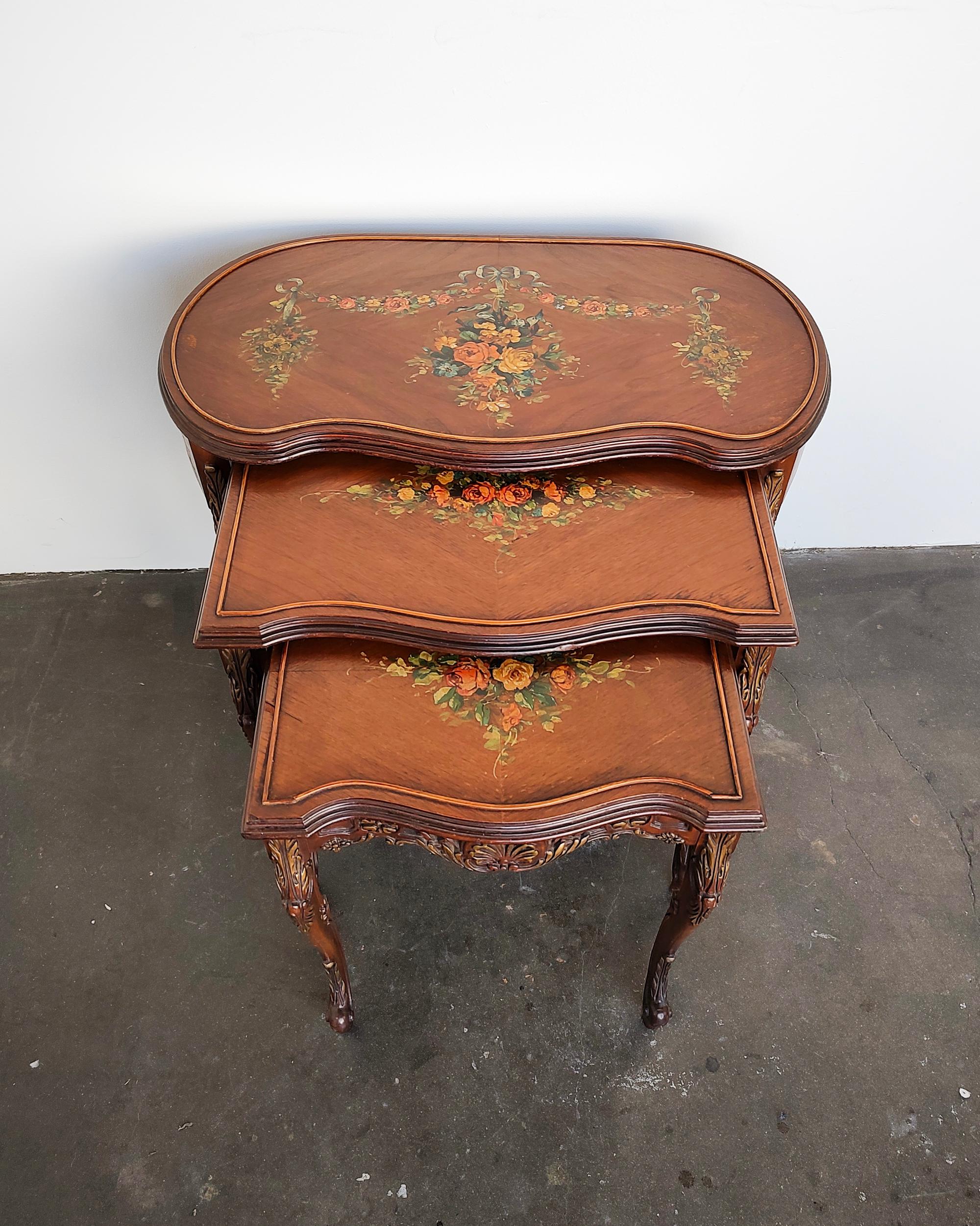 Set of three early 20th-century French Louis XV style wood nesting tables. Hand painted floral design on top, delicate curved legs and carved details with light gold embellishments. Overall great original condition, typical wear consistent with age.