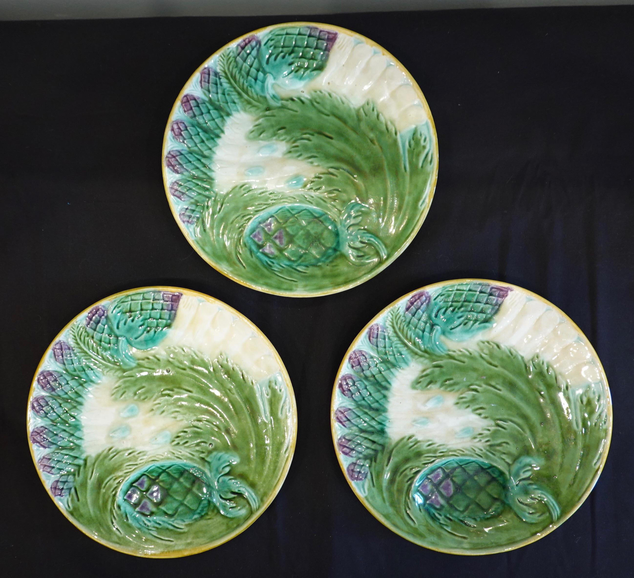 Set of three French Majolica asparagus plates by Saint Amand, (19th century). Each plate features a molded design of seven asparagus spears with an artichoke and acanthus leaf, with a depression for lemon or sauce. One plate is stamped Saint Amand,