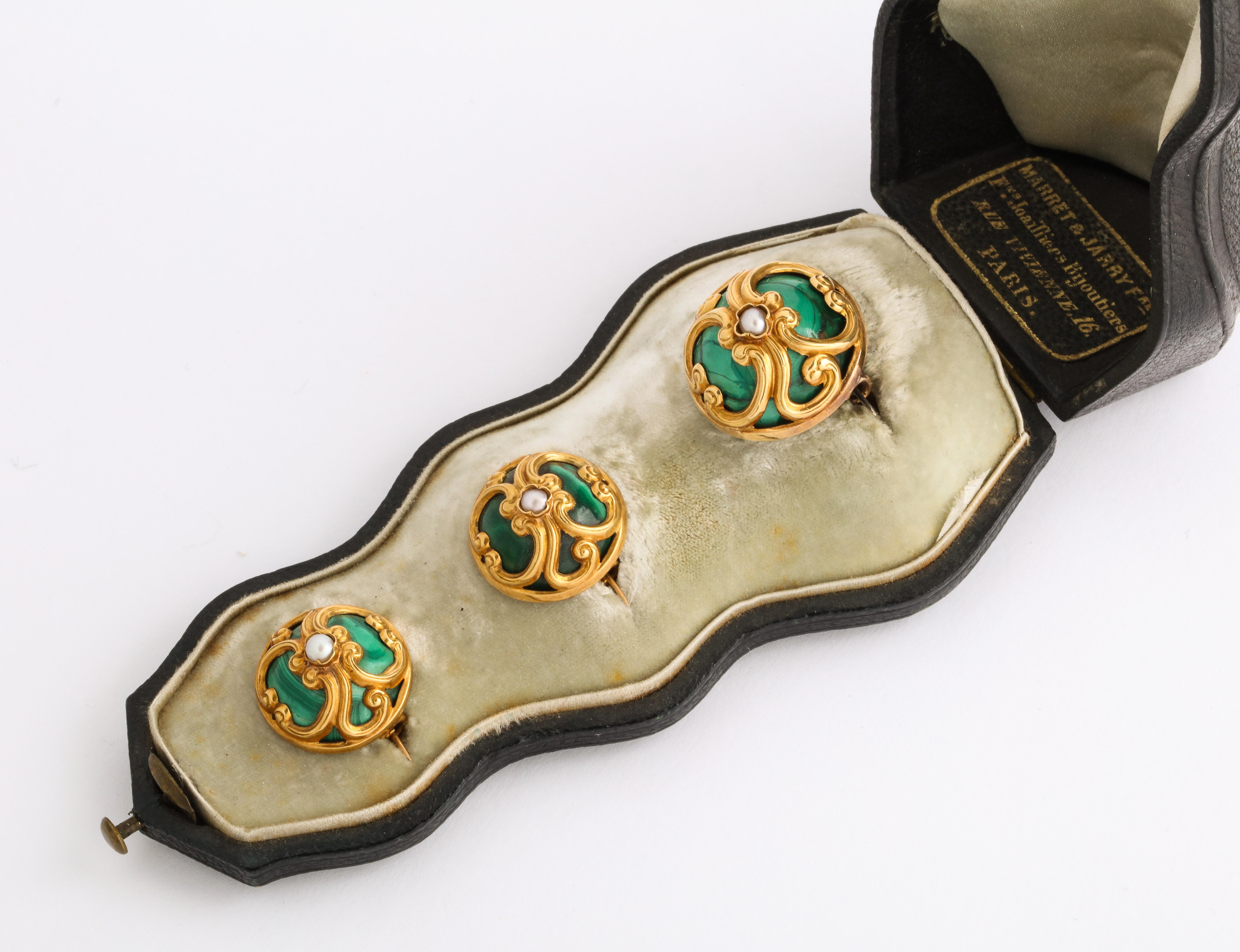 In the Louis XVI taste, a rare set of three French malachite 18k gold domed pins, one larger and a pair of matching, the tops tooled in gold tracery workshops of Paris, each enhanced by a central pearl, in original fitted leather case stamped Marret