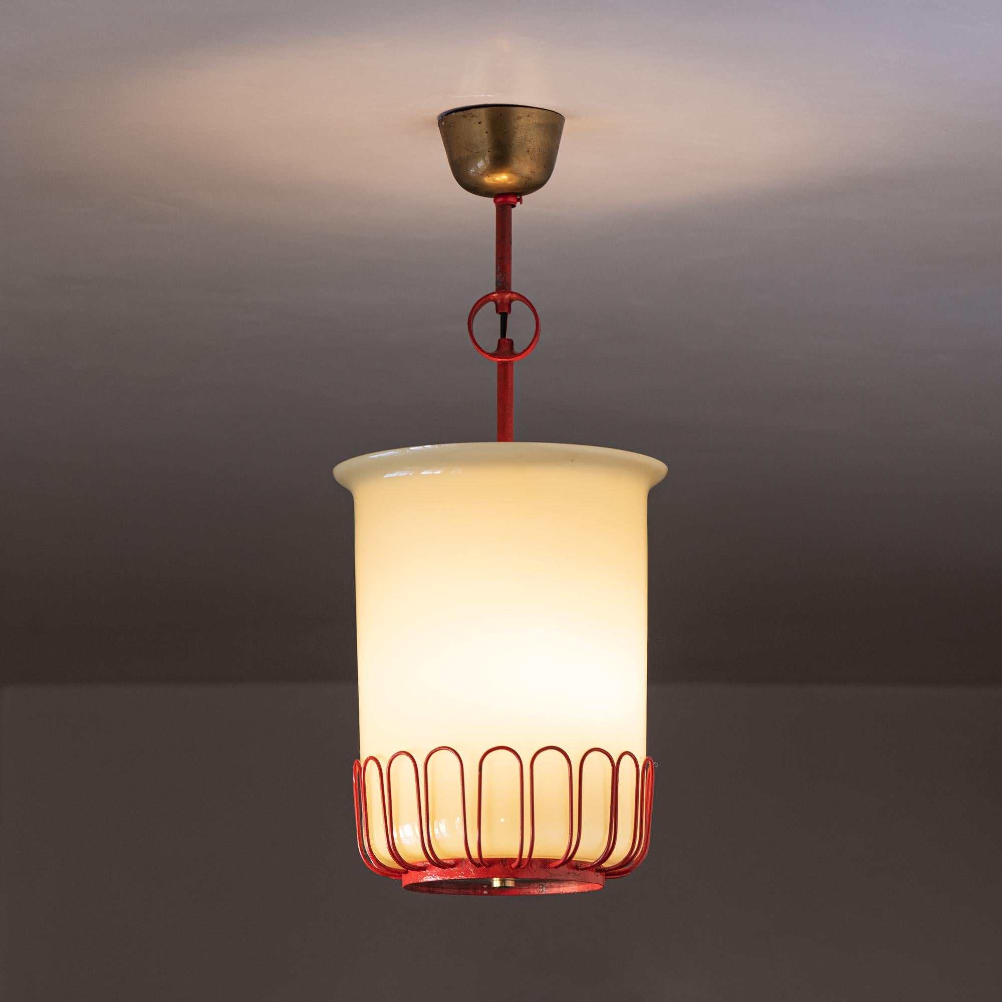 A stunning set of three French pendants reminiscent of the lights of Jean Royere. 
 These examples in red lacquered metal with brass accents and opaque off-white blown glass shades. France, 1950s.