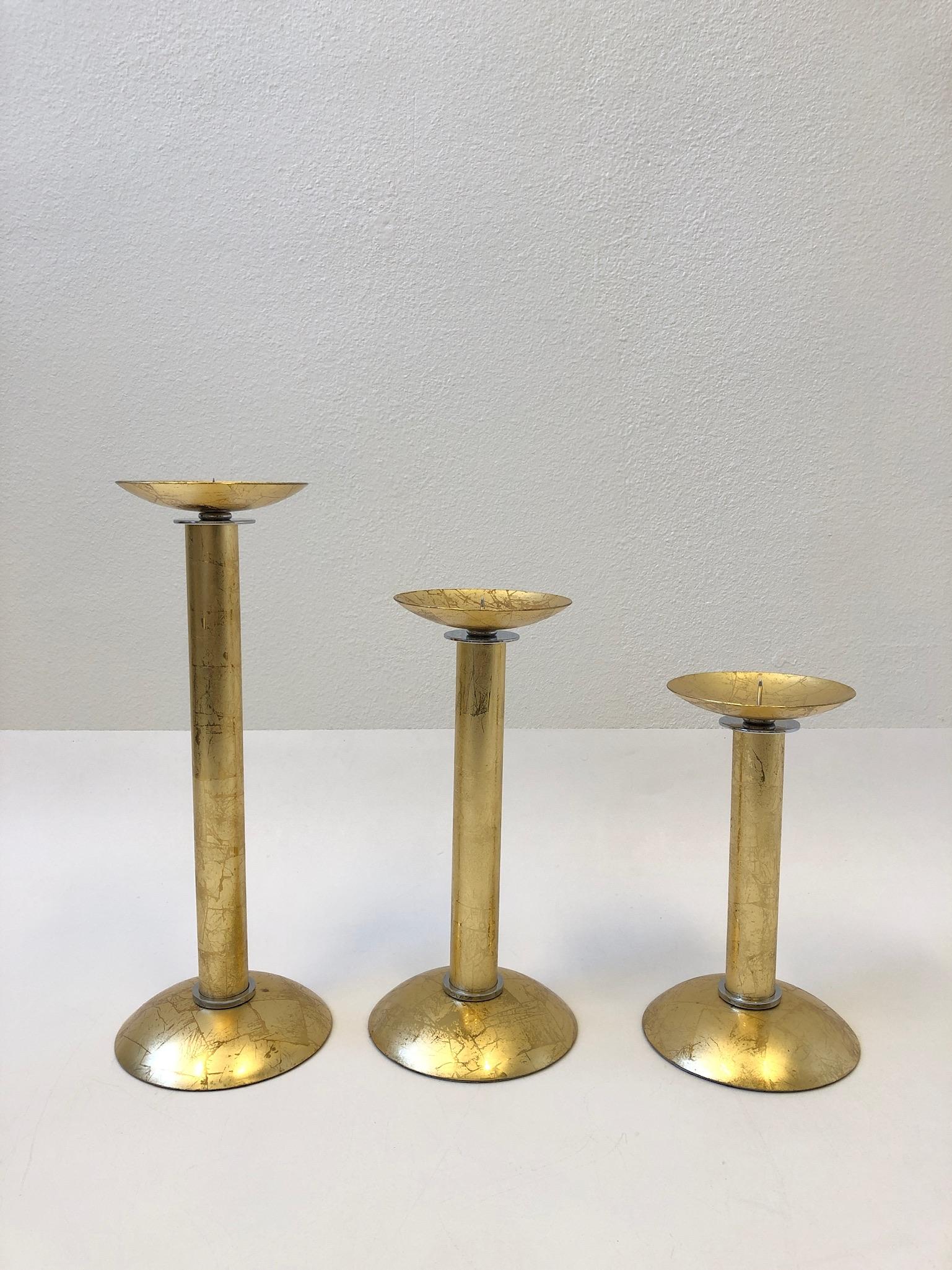 A glamorous set of three gold leaf brass and chrome candlesticks design by renowned American designer Karl Springer in the 1980s. The gold leaf brass finish is very unusual as they are usually polish brass. The candlesticks are in original