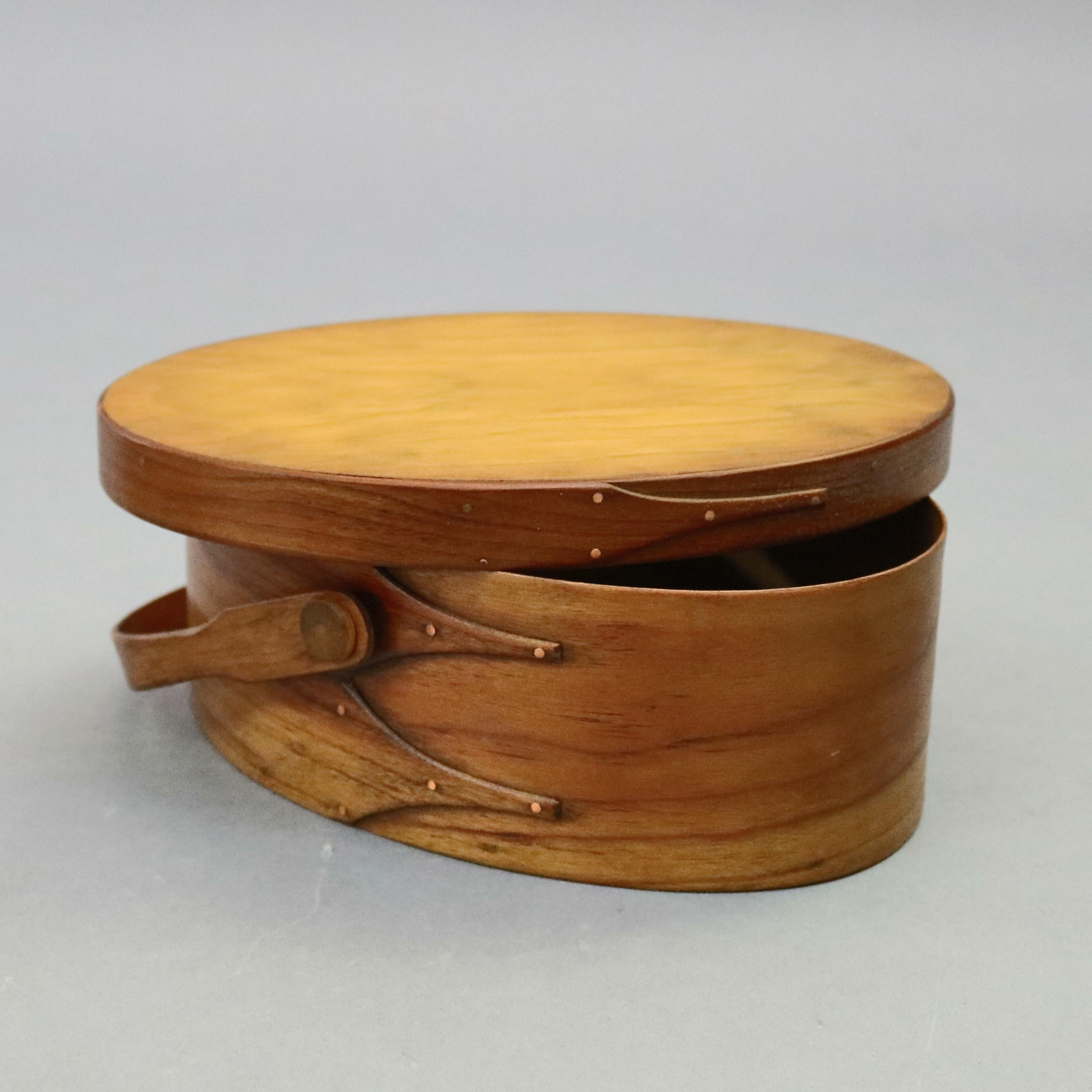 Three Lesher school shaker graduated, lidded boxes offer bentwood maple and cherry pegged construction in oval form with Gothic-shaped finger joints (swallowtails) finished in copper tacks, two with swivel handles and one without, 20th
