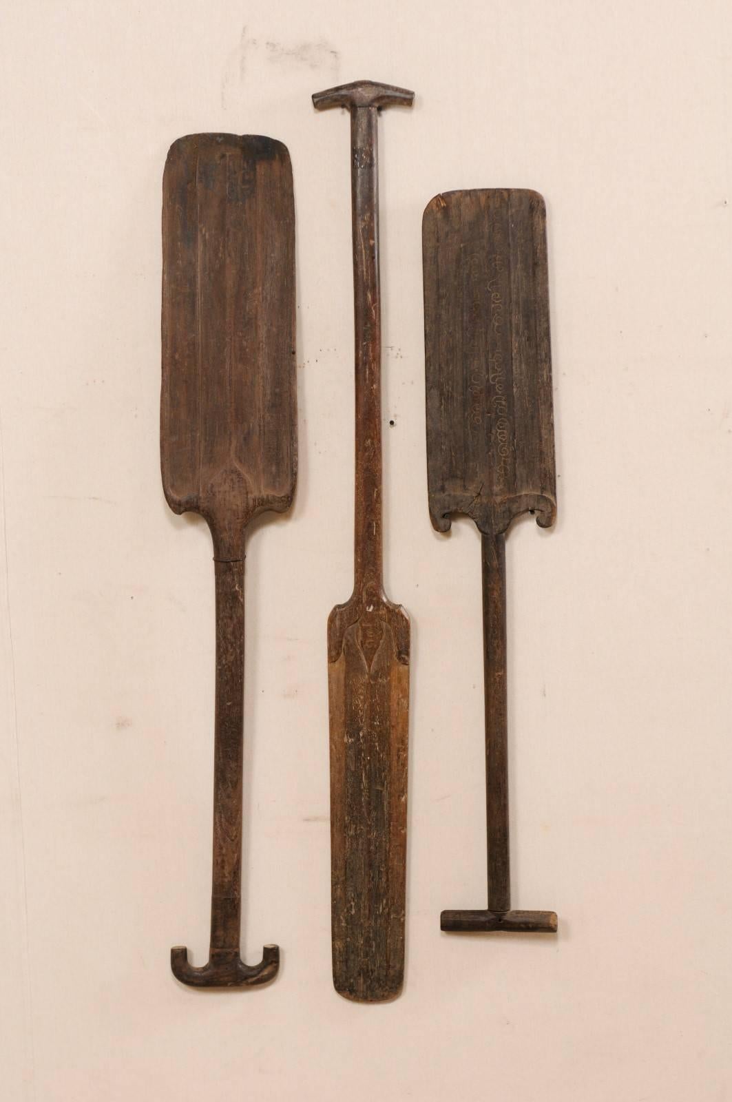 A collection of three South Indian (Kerala) wooden boat paddles from the mid-20th century. This collection of hand-carved boat oars from Kerala are each adorn with decoratively carved accents at the top of the blade, and slightly differing carved
