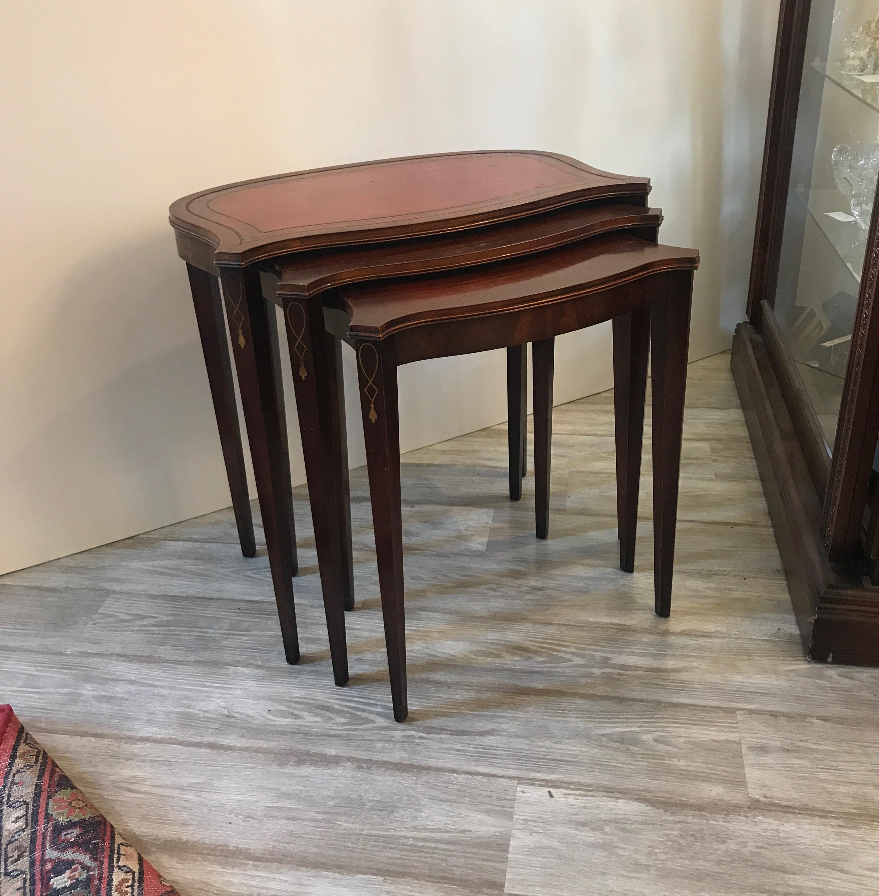 A set of three mahogany nesting tables. The largest with a tooled leather top. The shapely tables with tapering legs with nicely inlaid decoration.