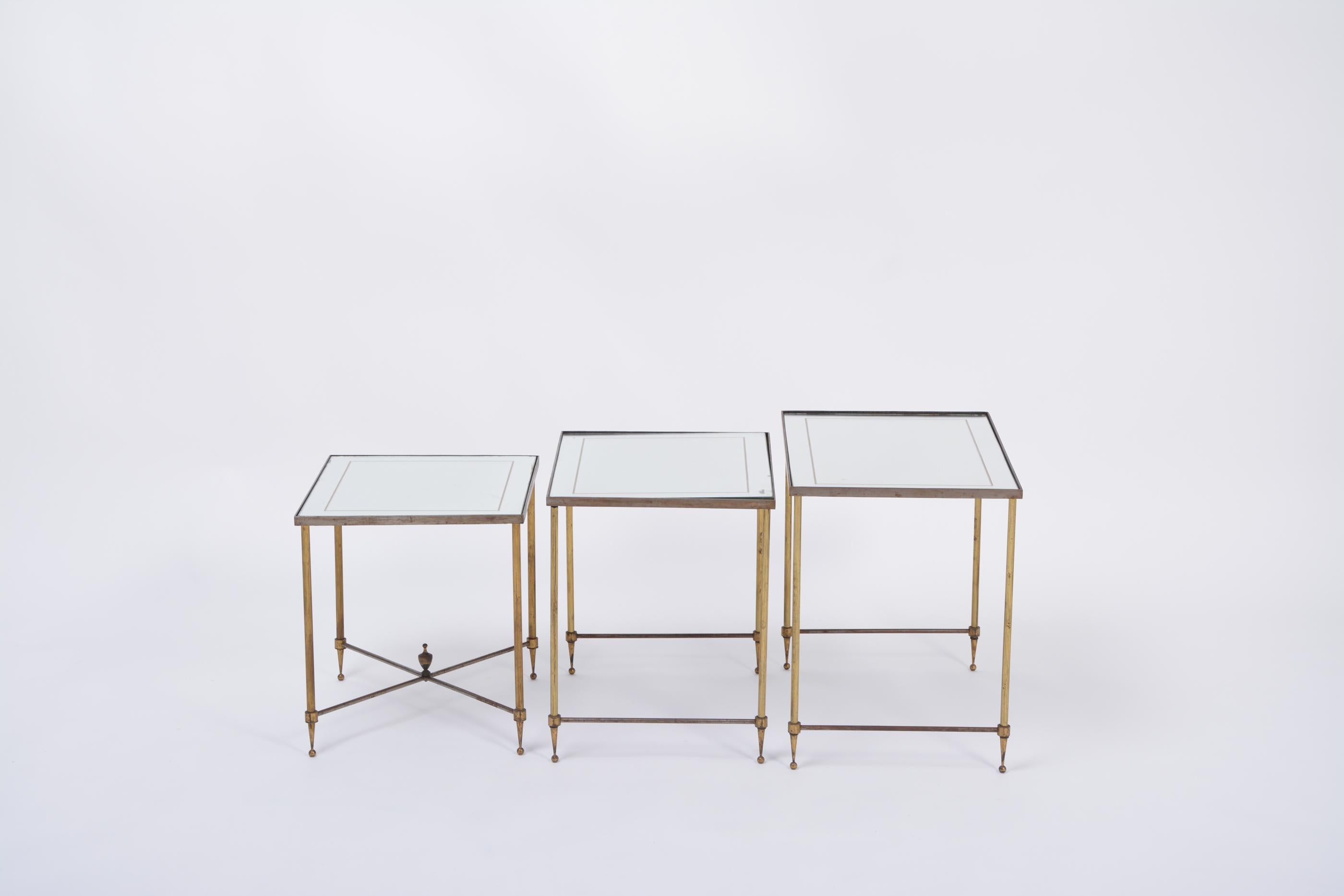Beautiful set of three Italian Maison Jansen style nesting tables with neo classical features. The tables are made of metal and feature mirrored tops with beautiful patina. Each table is supported by four thin and elegant reeded legs, raised on
