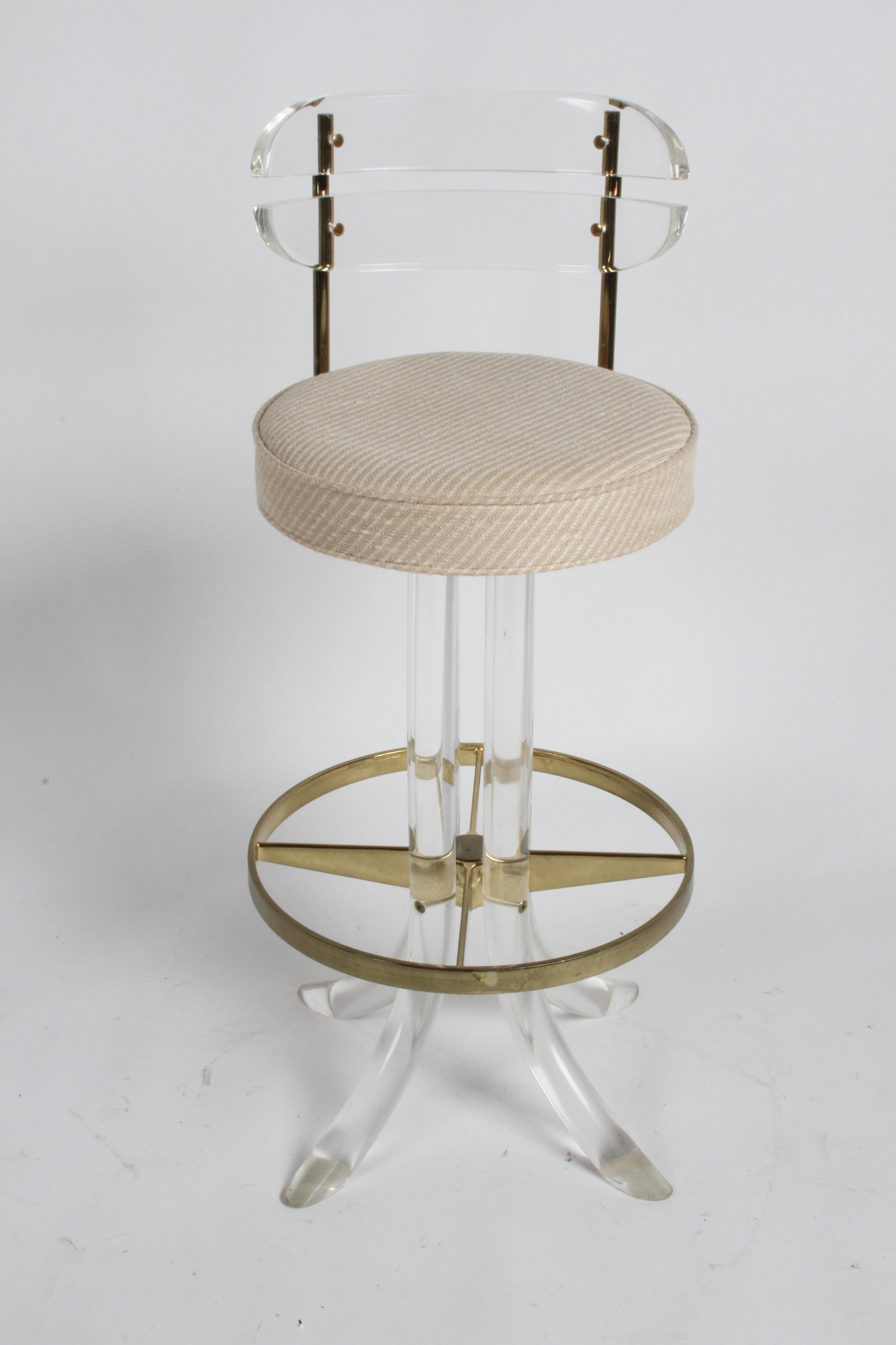 Beautiful set of three 1970s Hollywood Regency Lucite and brass bar stools with backs, foot rest and swivel by Hill Manufacturing Corp of New York. Original salmon and creme upholstery in fine condition, on thick round Lucite splayed legs. Brass and