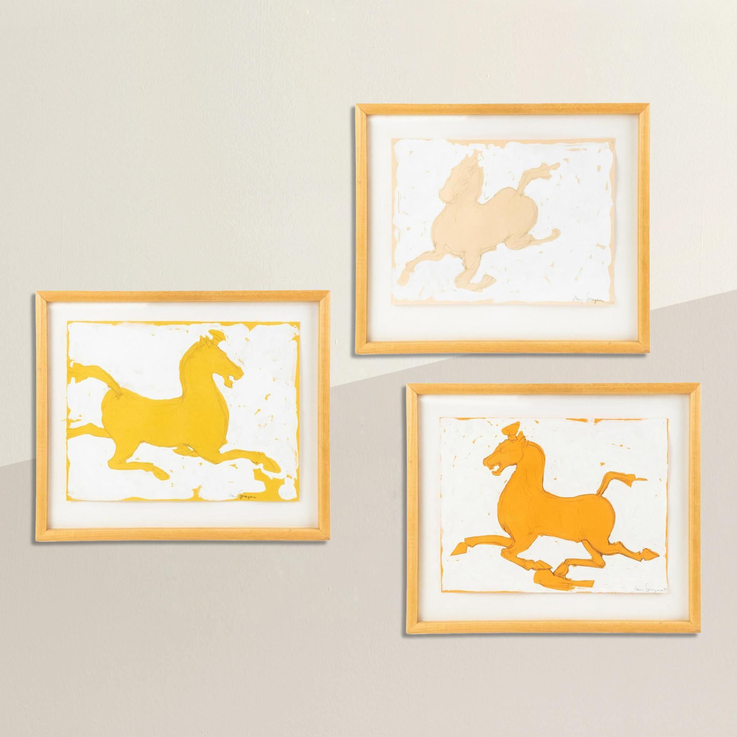A set of three playful horse paintings by Mary Sprague, dated 1988. Each painting is rendered in graphite and white paint against yellow and orange papers, and floated in simple maple gallery frames and under glass.