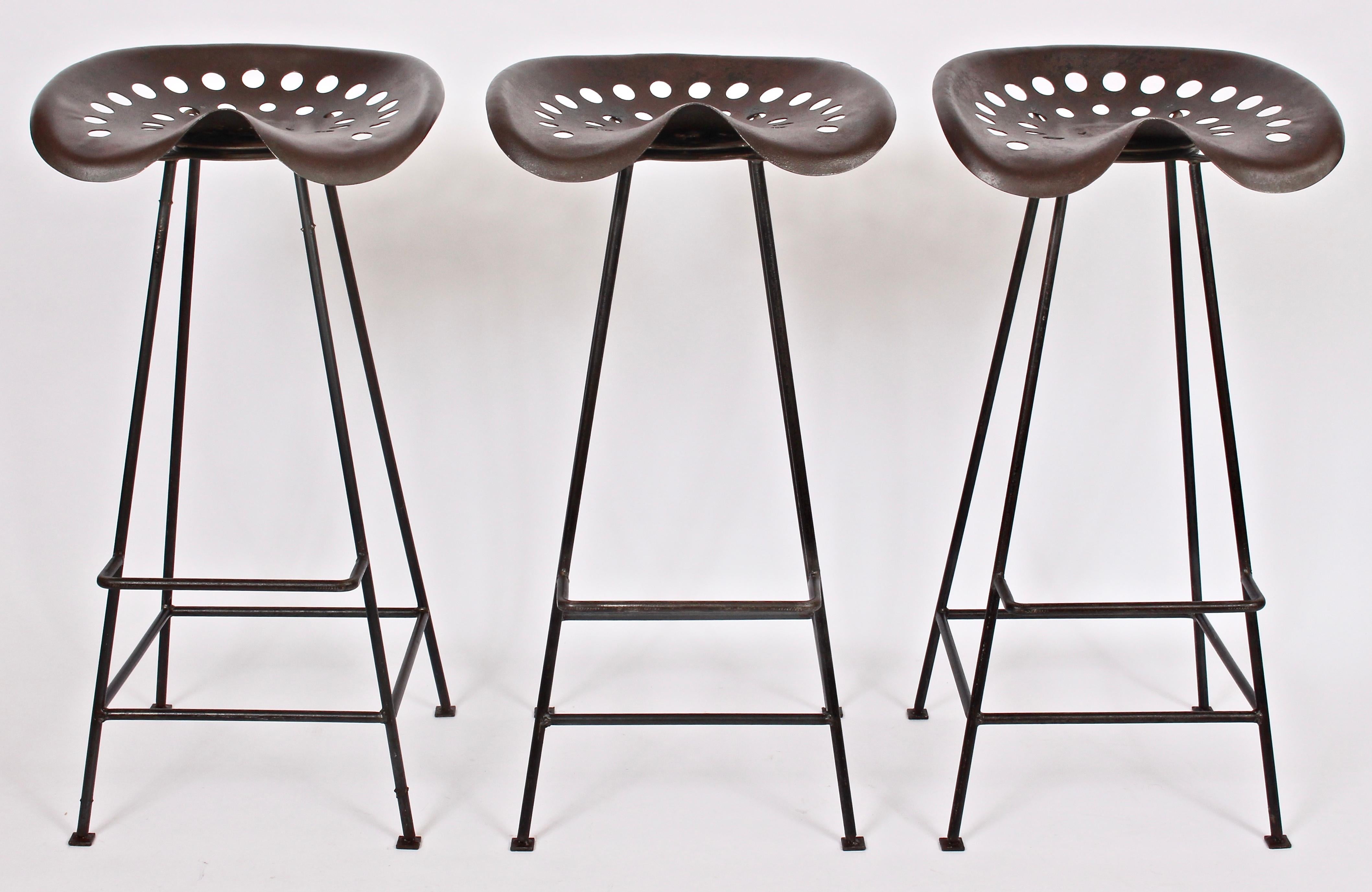 Trio of American Mid Century handcrafted tractor seat bar stools. Featuring a sturdy, open Iron framework, footrests with wide perforated patinated and sealed swivel seats (17