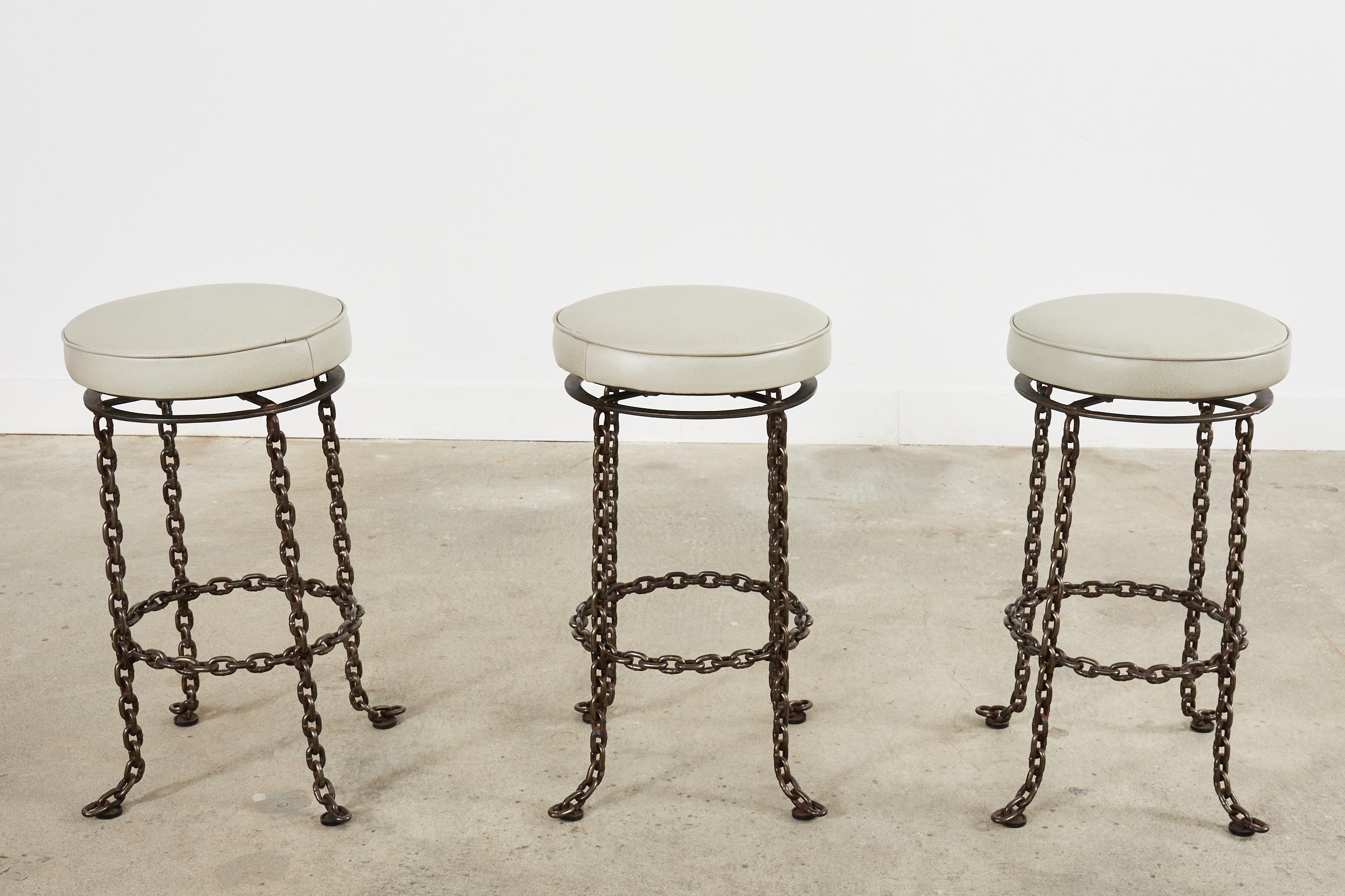 Chic set of three swivel barstools featuring an industrial style sculptural iron chain link base. Each stool is hand-crafted from thick, chunky welded chains having four legs that are splayed at the end. The legs are conjoined by a round stretcher