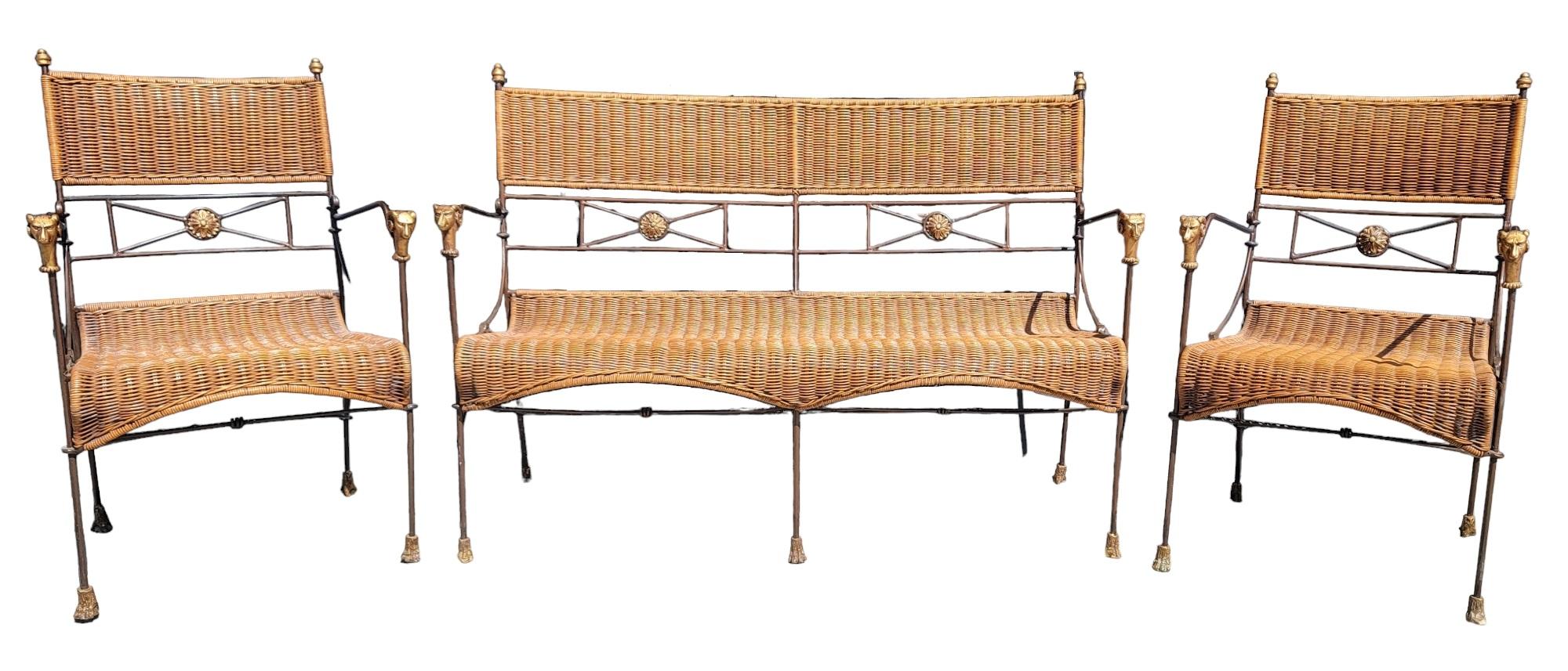 Set of Three Iron And Wicker Settee And Chair By Giacometti. There are rams heads on the arm rests. In the back rest there is a sunburst/sunflower emblem/design on the backing. 
The top of the chairs have small finials attached. The iron under the