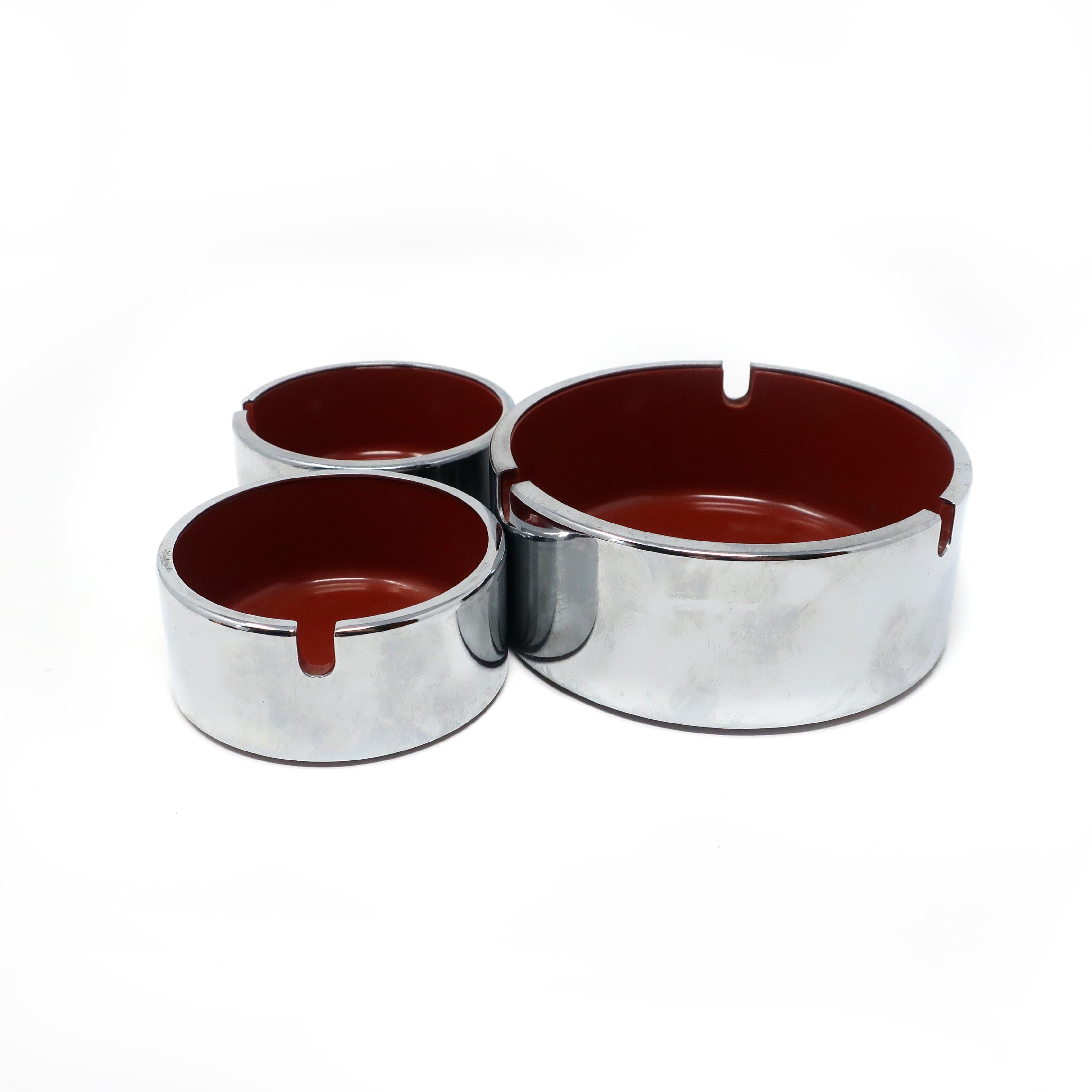 Set of three perfectly Mid-Century Modern plastic and chrome ashtrays designed by Isamu Kenmochi. All three are maroon; one is the medium size and the other two are the small size. In excellent vintage condition with no scratches or cracks.