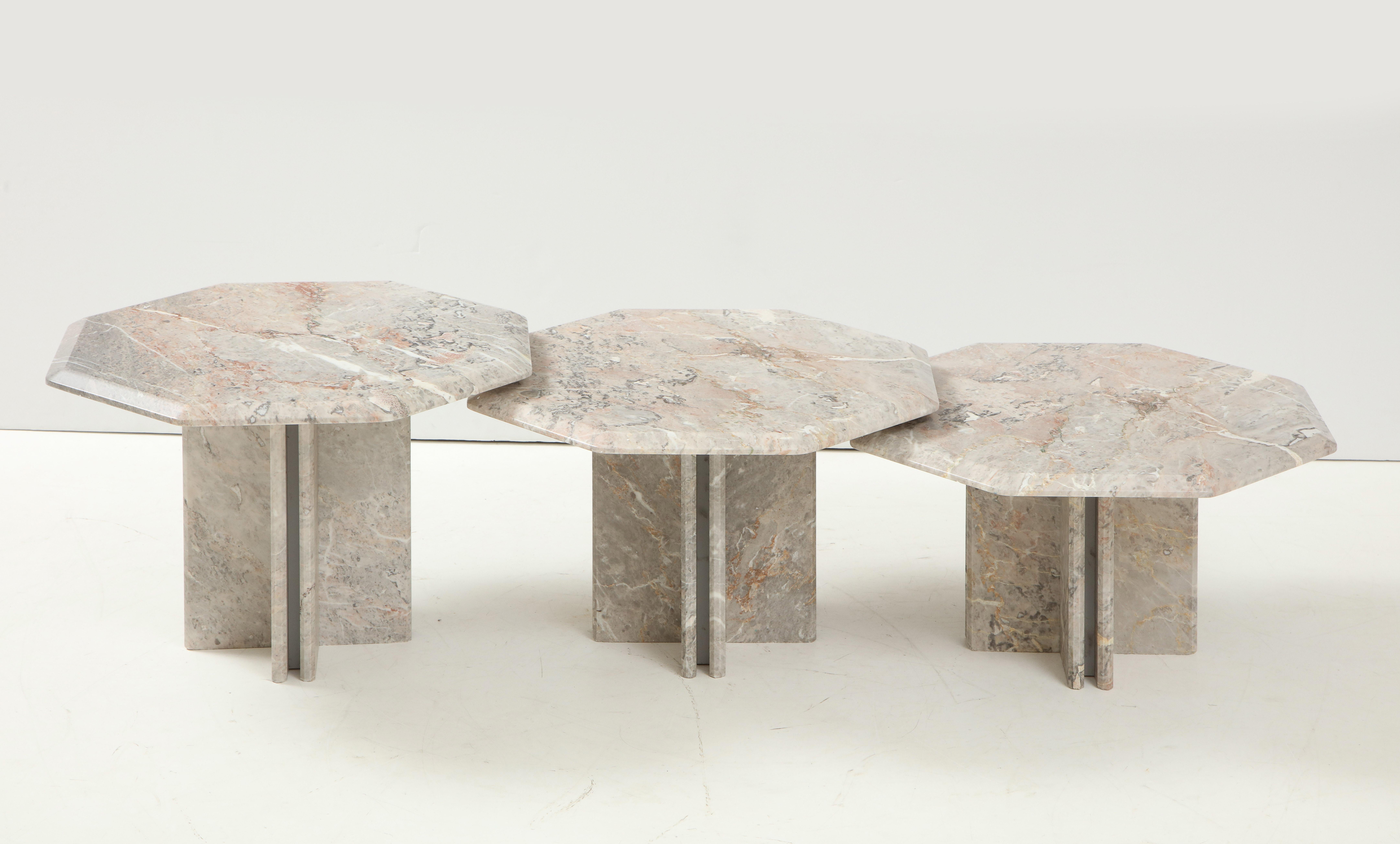 A set of three marble nesting tables, the tops are cut in an octagon shape and are graduated in height. The tops are supported on four sided bases. The vein of the marble is a beautiful and warm grey, cream, white and pink. Can be displayed