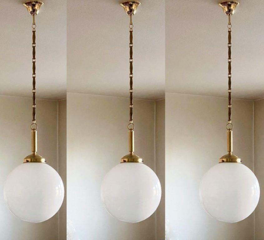 A set of three hand blown opaline glass ball pendant with brass mounts, chain and canopy, Italy, 1940s.
One porcelain Edison E-27 light socket for a large sized screw bulb up to 100W.
Measures: Diameter 12