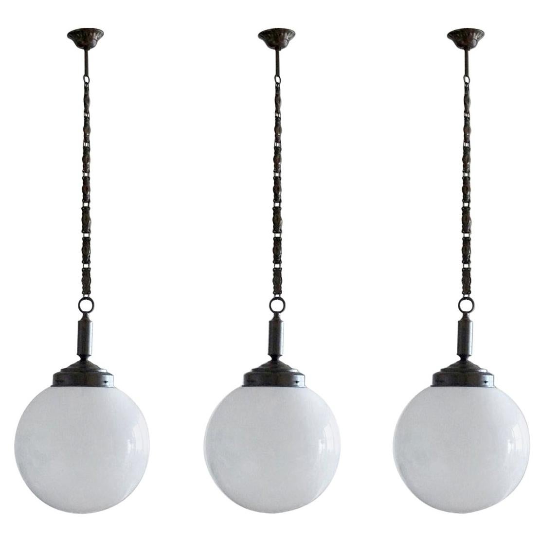 A set of three hand blown opaline glass ball pendants with burnished brass mounts, chain and canopy, Italy, 1930-1939.
One brass Edison E-27 light bulb socket for a large sized bulb up to 100W.
Measures: Diameter 12