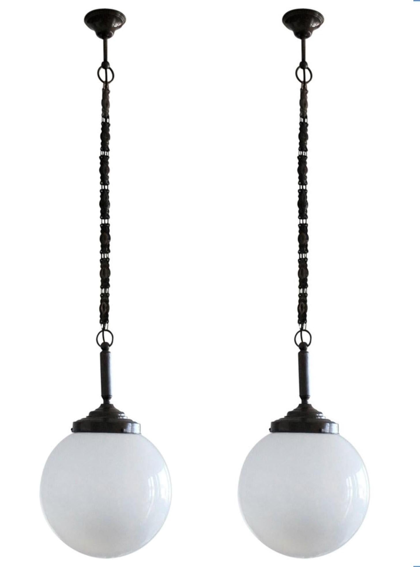 A set of three hand blown opaline glass ball Theatre pendants with burnished brass mounts, chain and canopy, Italy, 1930-1939. With a single Edison E27 light socket for a large sized srew base bulb up to 100W. LED bulbs can also be used. All three