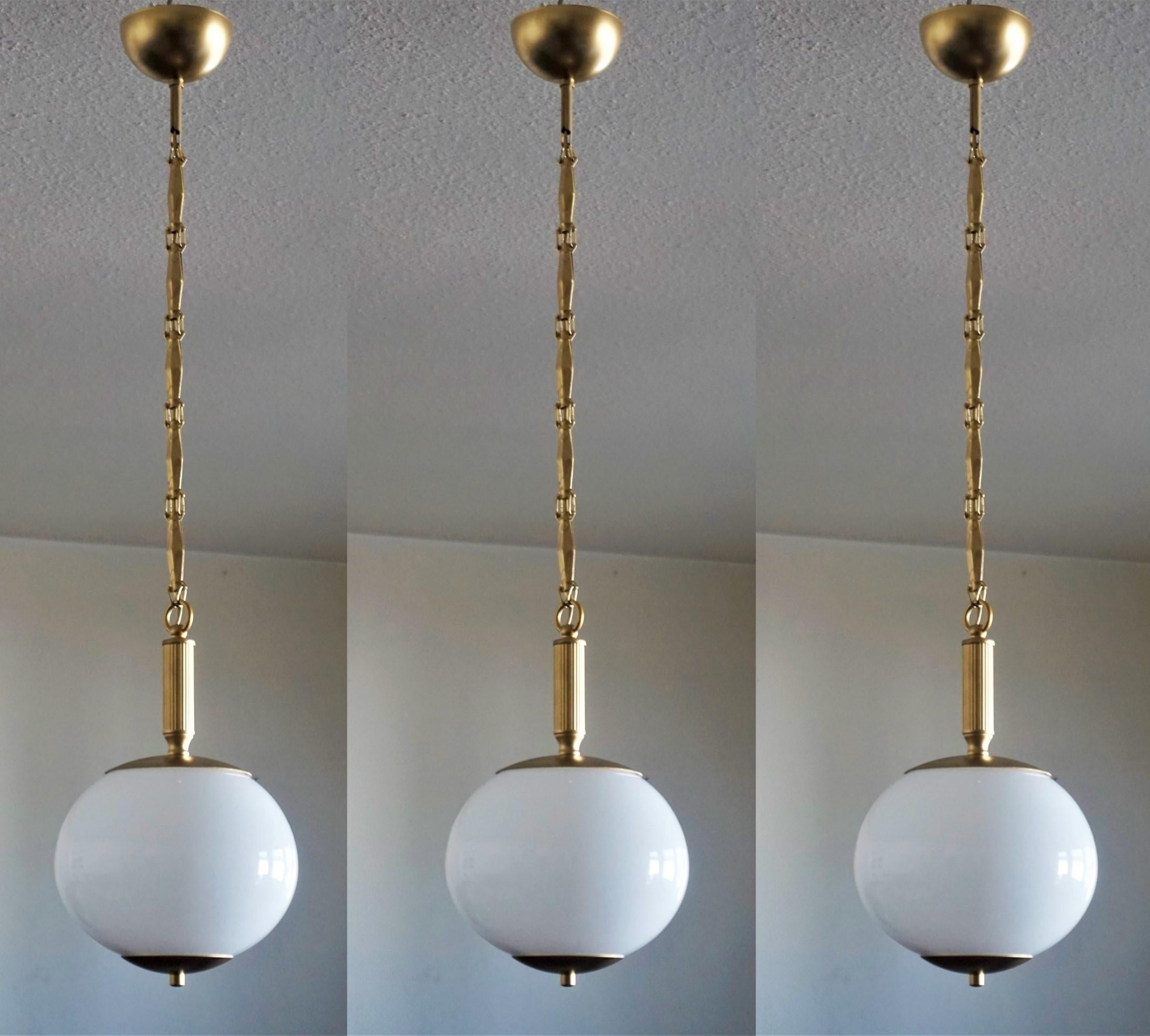 A set of three Italian hand blown opaline globe pendants, brass mounts, chain and canopy, 1950-1959.
With a single brass and porcelain Edison E-27 light socket for large sized bulb (each pendant).
Measures: Height 33 in / 84 cm, adjustable by