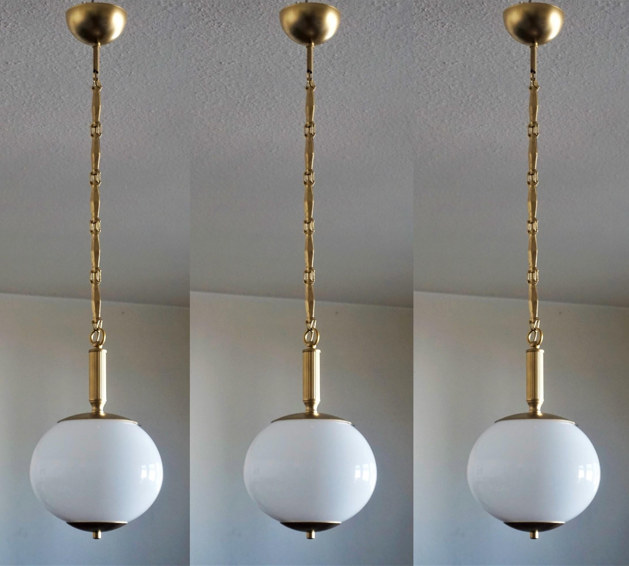 Juego de tres colgantes italianos globo de opalina soplados a mano, monturas de latón, cadena y dosel, 1950-1959.
Con un único portalámparas Edison E-27 de porcelana para bombilla de gran tamaño (cada colgante).
Medidas: Altura 104 cm, ajustable