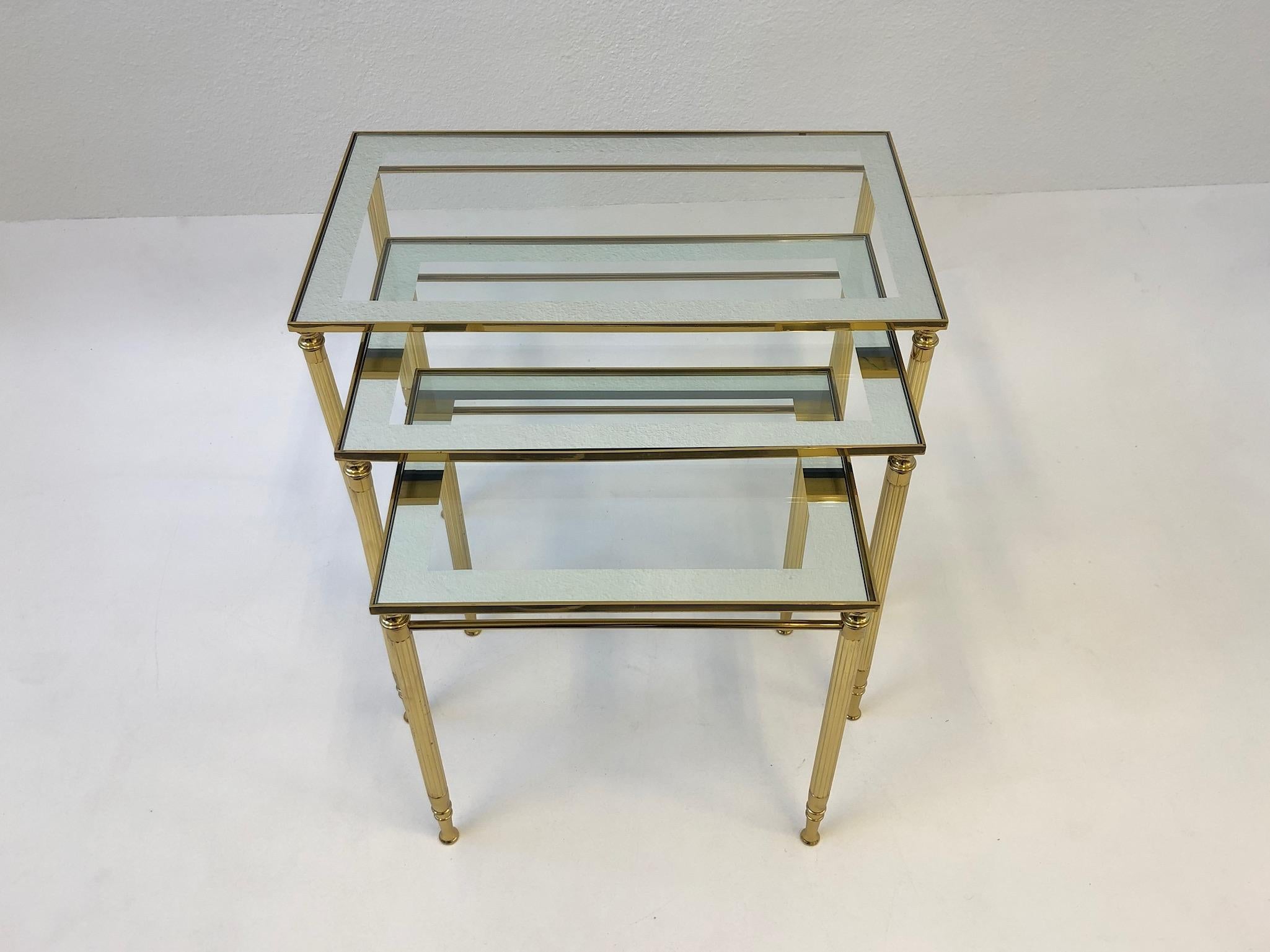 Glamorous 1970s set of three Italian brass and mirror frame glass tops nesting tables by Maison Baguès. The tables are constructed of solid brass with mirror frame glass tops. They are in original condition, so they show minor wear consistent with
