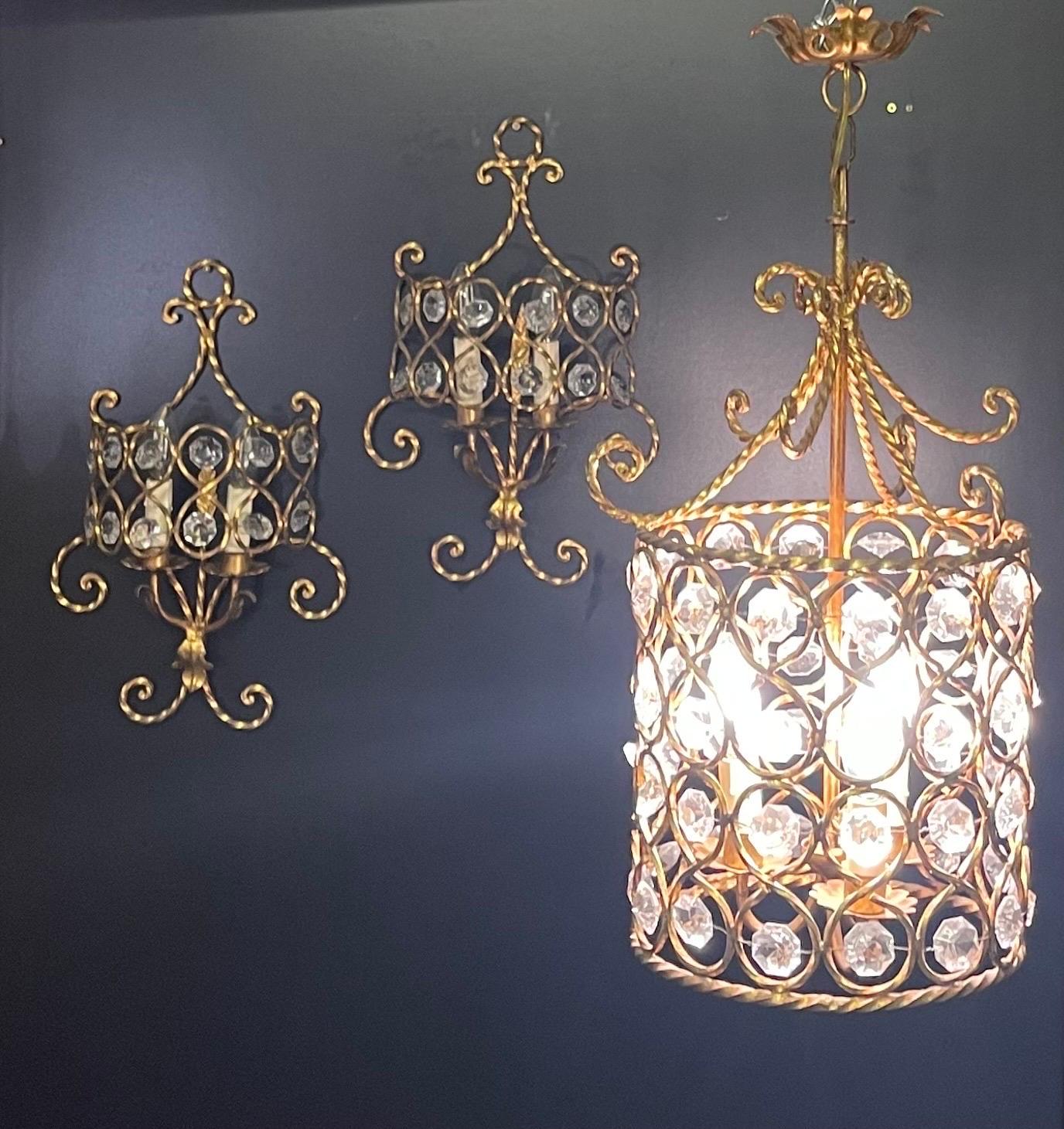 Set of three Italian gilt iron and crystal light fixtures ( lantern and a pair of wall sconces), circa 1950s.
Dimension of a lantern:
Height: 24.40 inches / Diamater: 11.81 inches.

Sconces:
Height: 18.50 inches / Width:24.40 inches/ Depth: