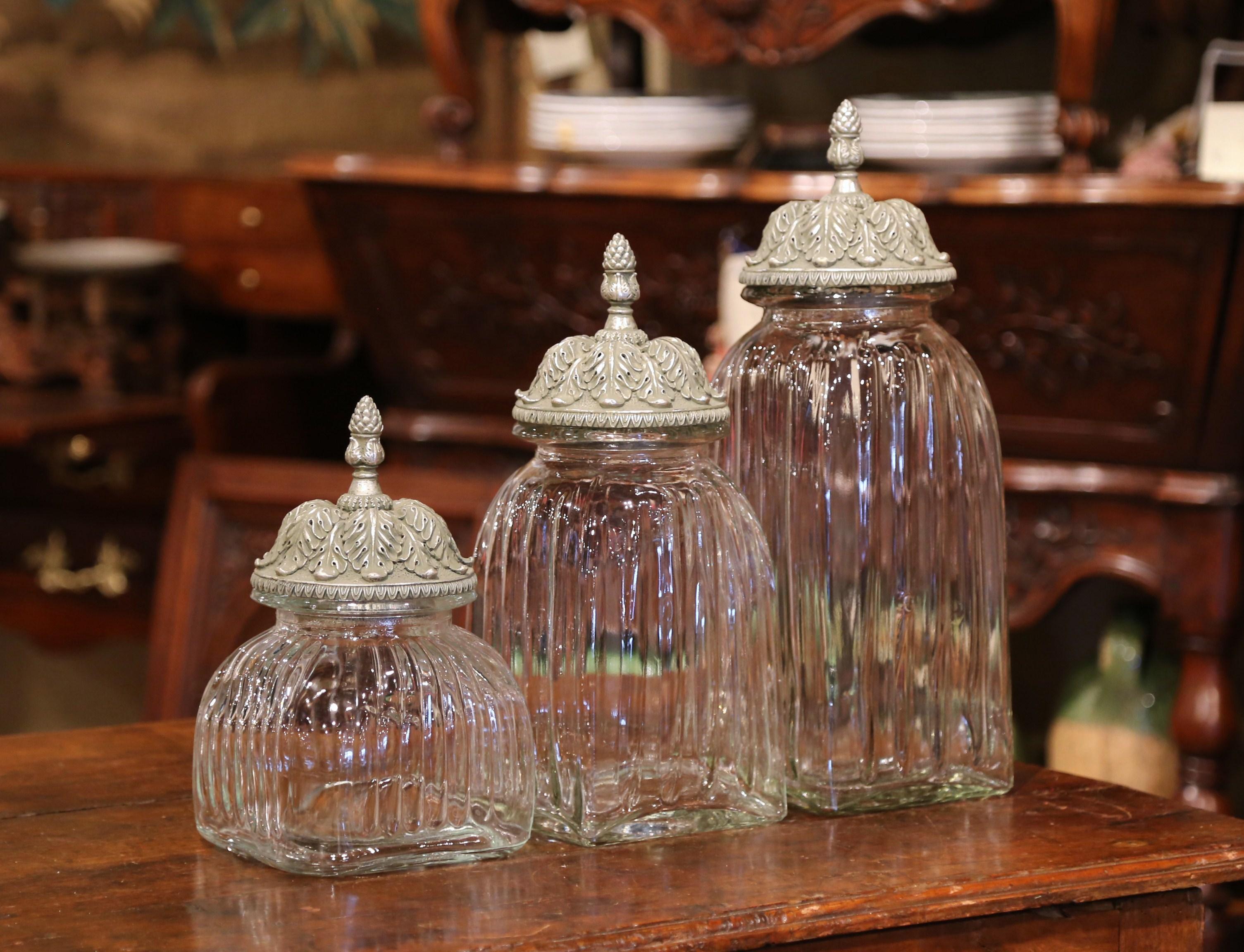 This versatile set of three Italian glass jars could be used in almost any room in your home. Crafted in Italy circa 1980, the graduated, glass jars have carved silver lids with a pine shaped finial, and wavy clear glass containers. The jars could