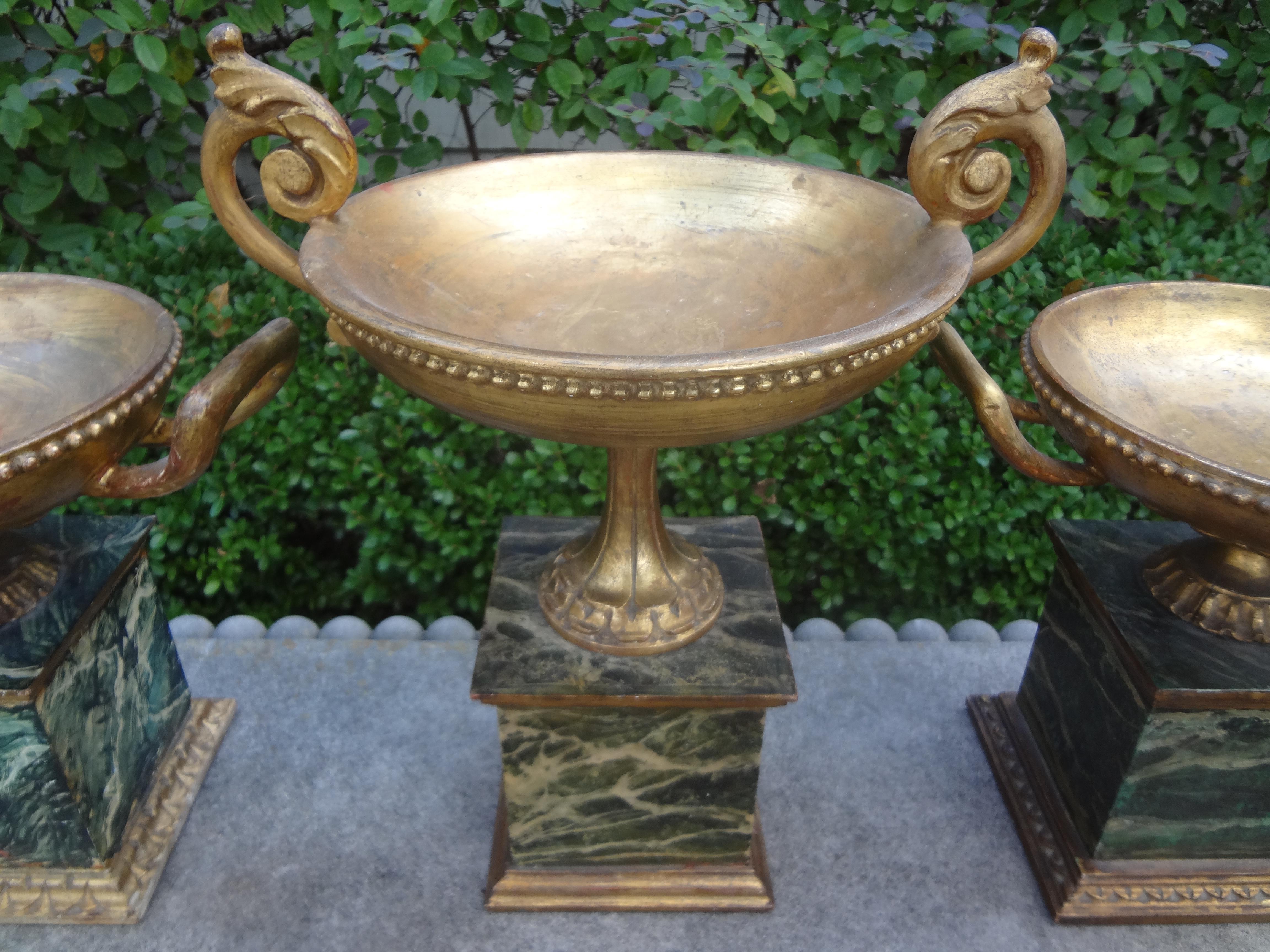 Beautiful set of three Italian neoclassical style giltwood urns with faux marbleized wood plinths. These giltwood urns date to the 1920s but are in the style of 18th century, Italian. This beautifully carved set is possibly the work of