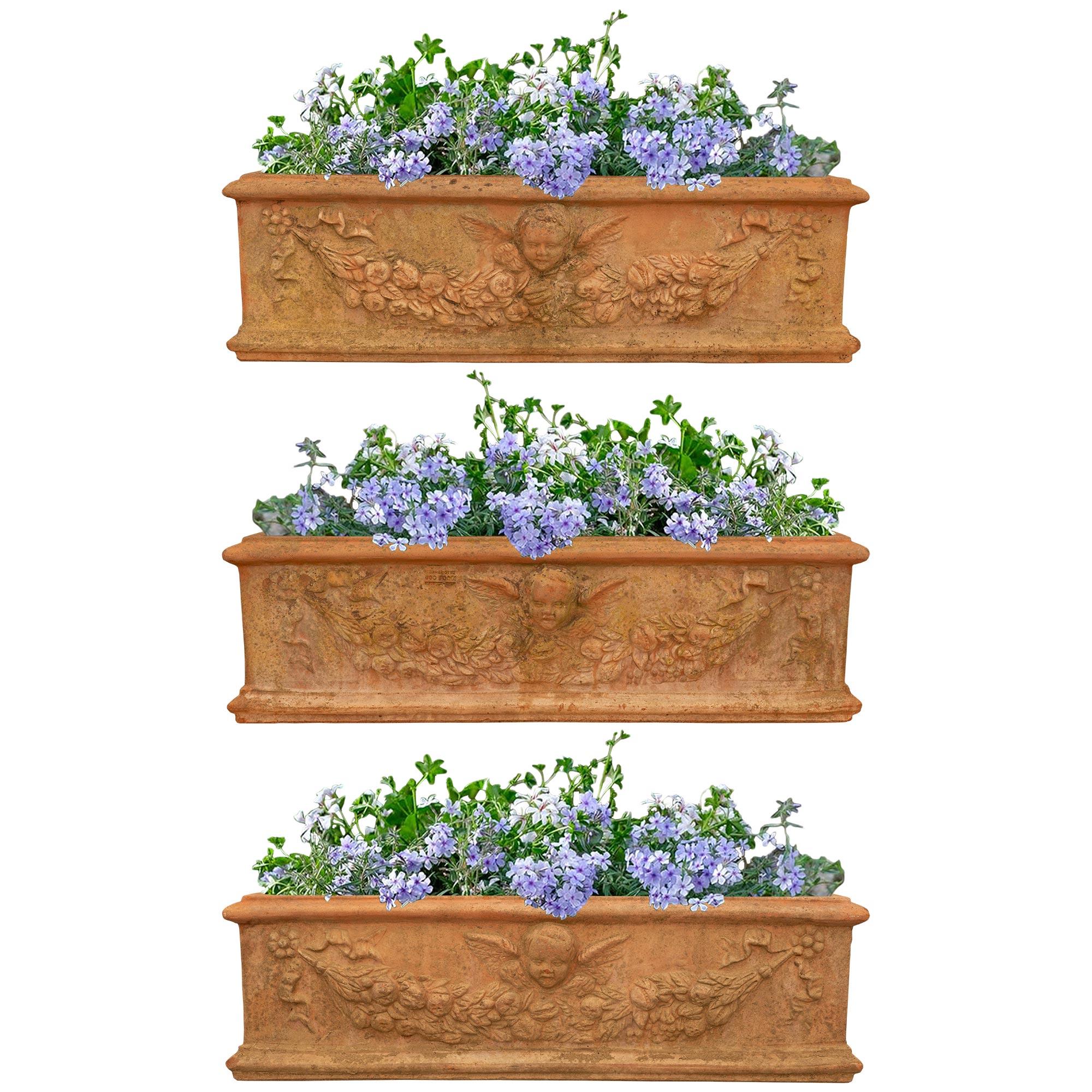 A charming and finely detailed set of three Italian Turn of the Century Tuscan st. Terra Cotta planters. Each wonderful planter is finished on all sides with a mottled bottom band below the central winged cherub. The cherub is above a swaging floral