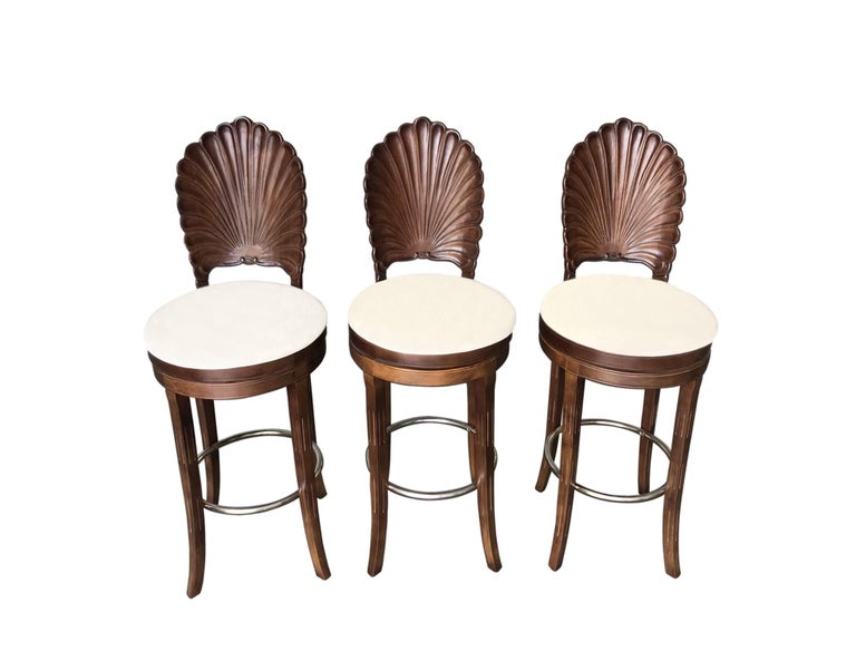 Three elegant Italian Venetian Grotto shell back swivel bar stools. Each chair was handmade with extra attention and features solid wood frames in a warm brown satin, scalloped shell motif back with cream color upholstered swivel seats. The splayed