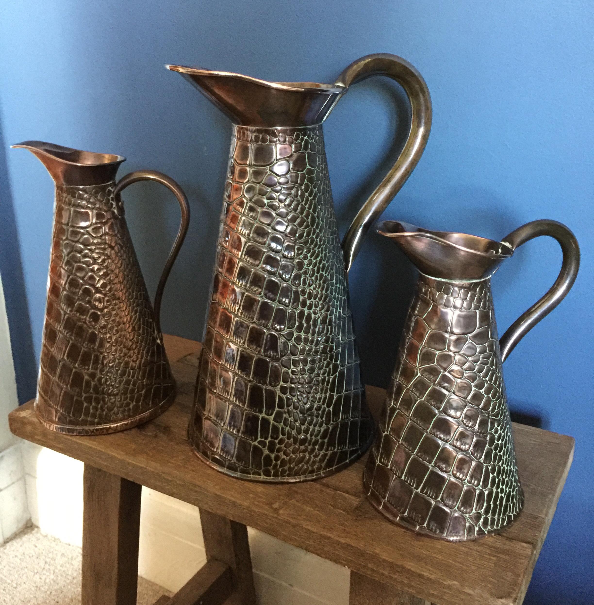 A wonderful graduated set of three Joseph Sankey & Sons copper jugs. Beautiful hammered Arts & Crafts crocodile skin effect outer. Nice to have a set and highly decorative. Stamped to base. The jug heights are 13