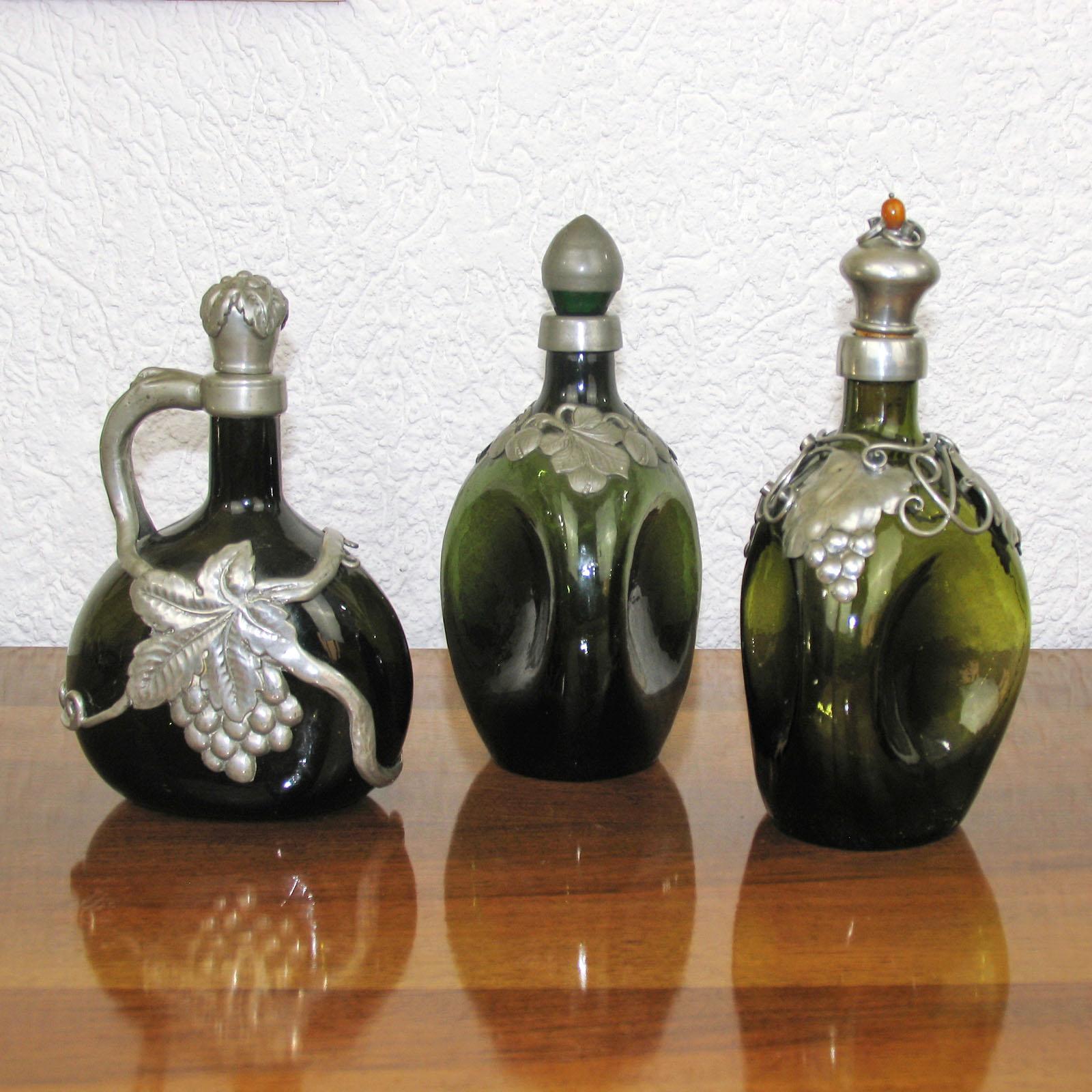 
Vintage decanter made of dark green glass decanter, with handle, stopper and embossed pewter overlay, wine and grapes decor. Very good used condition. After a design of Georg Nilsson.
Measure: Height 25 cm.

Triangular green glass bottle with