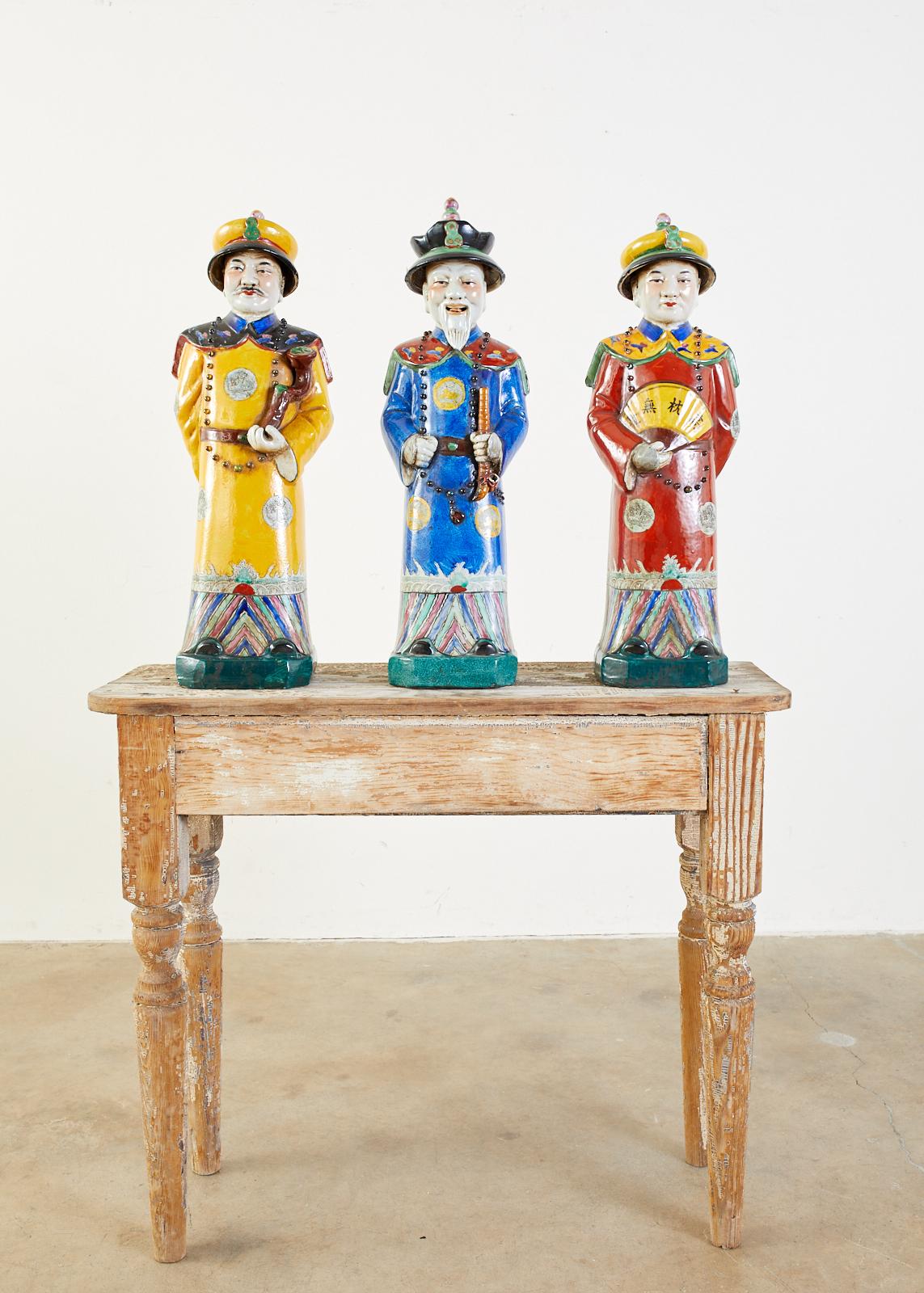 Colorful set of three large Chinese porcelain Qing emperor, royal, and monarch figural group. Beautifully glazed with a wucai style having flamboyant robes and hats. Decorated with beaded necklaces holding a flute, a fan, and a ruyi-head scepter.