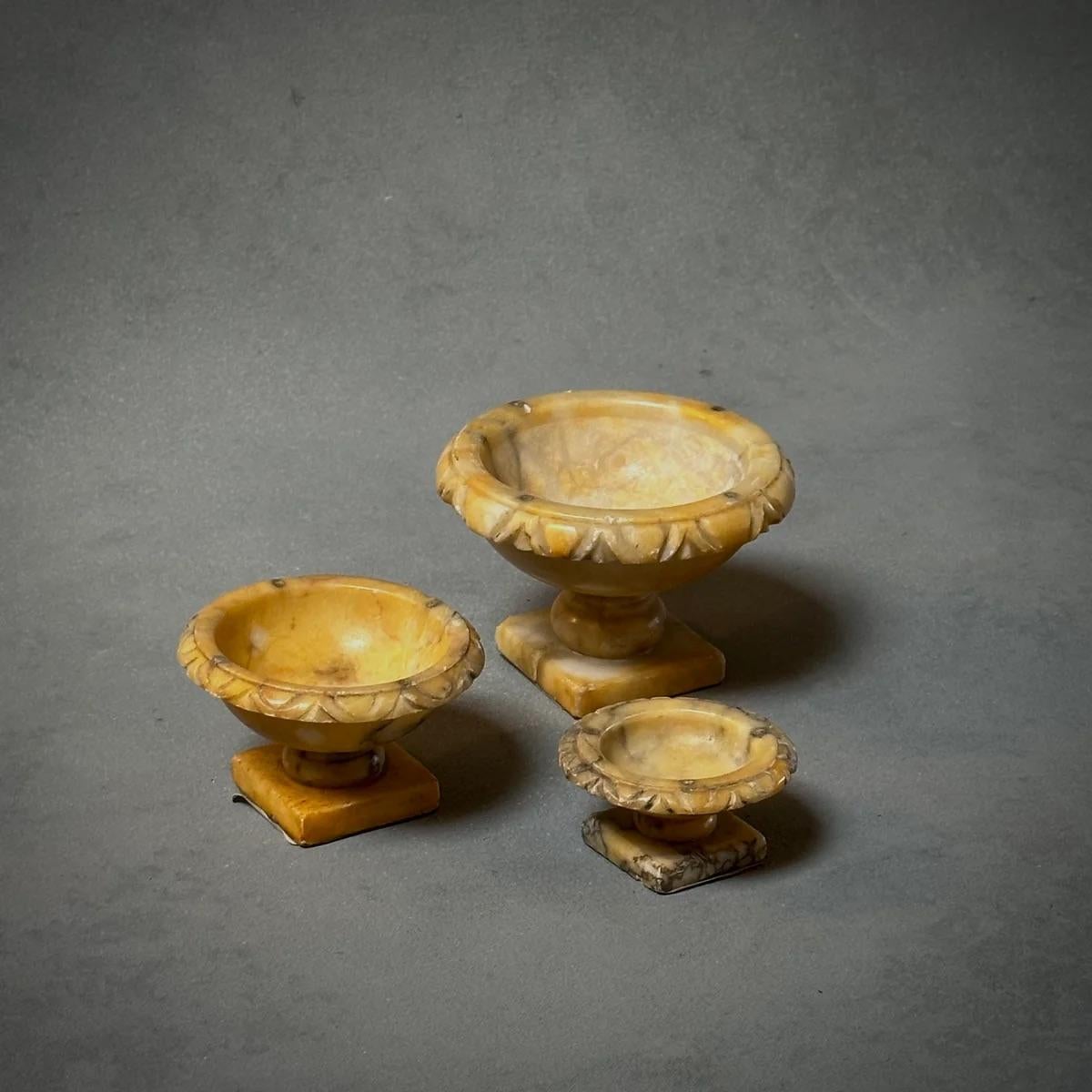 Ce trio de tazzas italiens en albâtre, avec leurs teintes ensoleillées et leurs bords classiques en forme d'œuf et de fléchette, est un témoignage de l'artisanat italien intemporel. Chaque pièce repose sur un socle carré, offrant des hauteurs