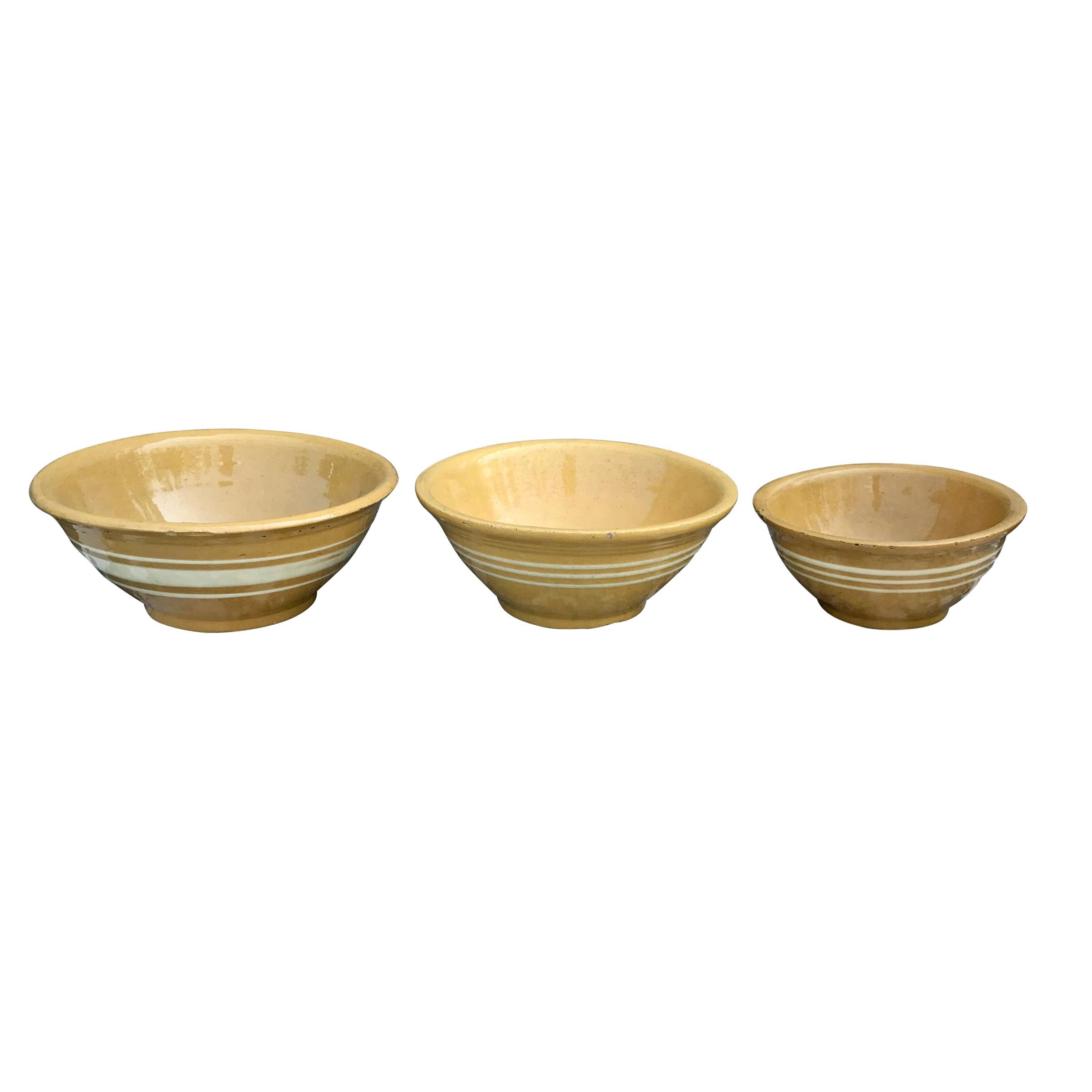 An assembled set of three late 19th century American yellow ware mixing bowls, two with three similarly sized embossed white glazed stripes and the largest with a wide embossed white glazed stripe flanked by two thinner embossed white glazed