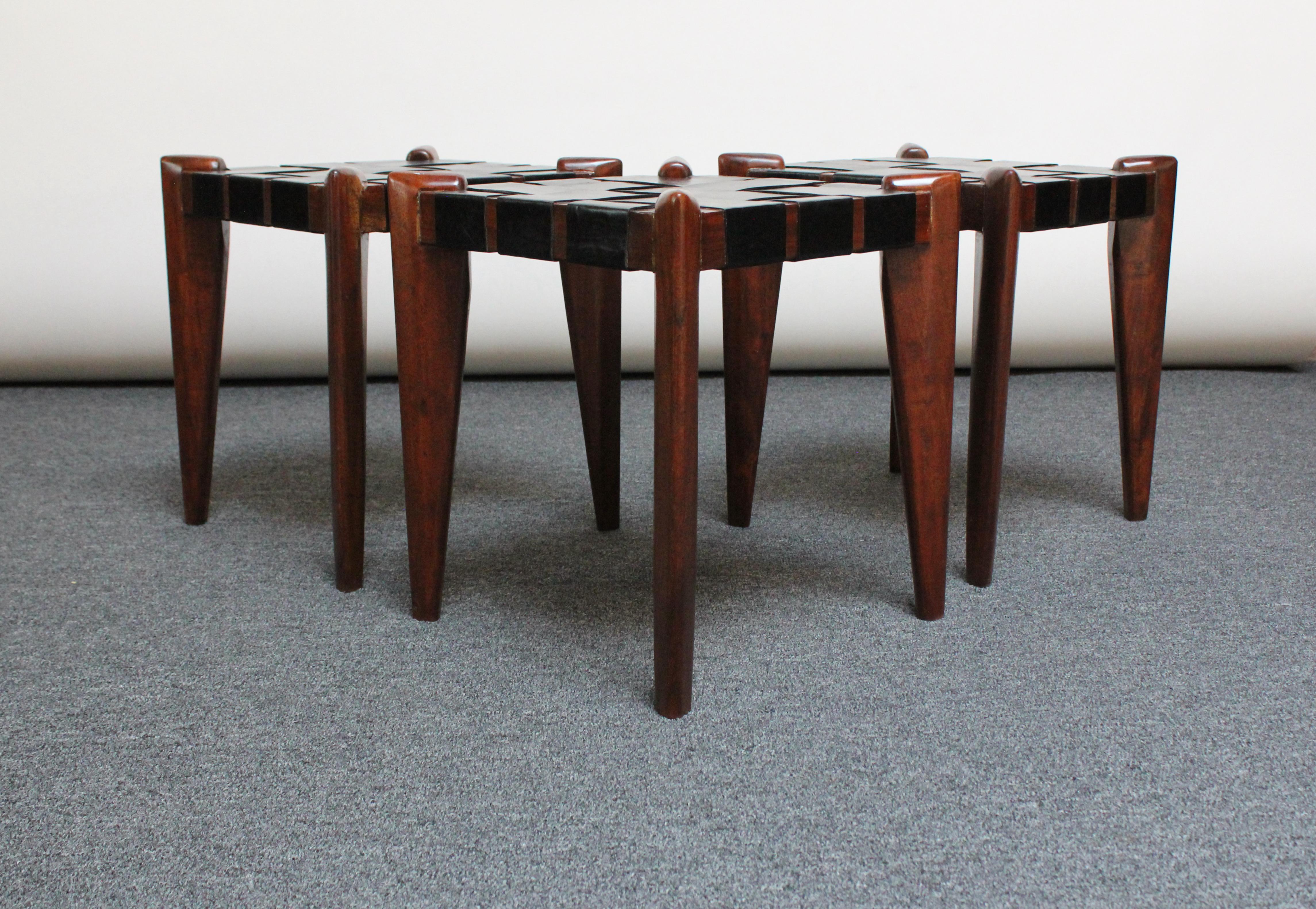 Sculptural teak wood stools with laced leather seats by Edmond Spence. Solid teak frames retain their original dark stain, and the leather is original. 
There is soiling and general wear to the straps' undersides from age and potentially storage.