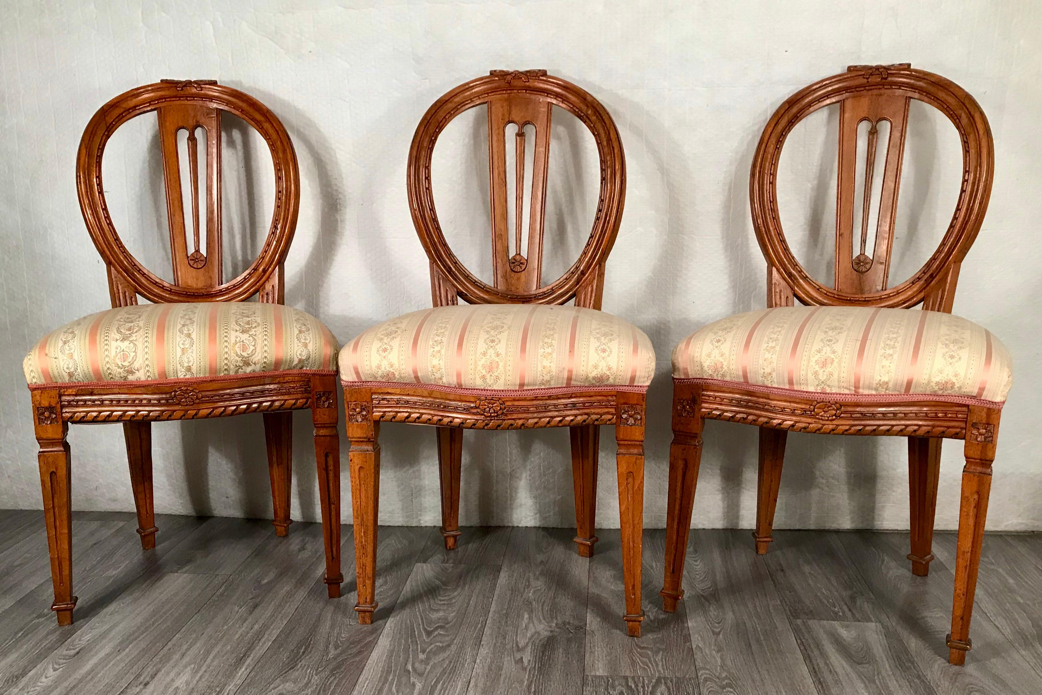 Satz von drei Louis XVI-Stühlen, Deutschland 1780-1800. Die Stühle sind aus Nussbaumholz, fein geschnitzt mit typischen Louis XVI-Motiven auf Rückenlehnen, Beinen und den Rahmen der Sitze. Die ovalen Rückseiten sind mit einer hübschen durchbrochenen
