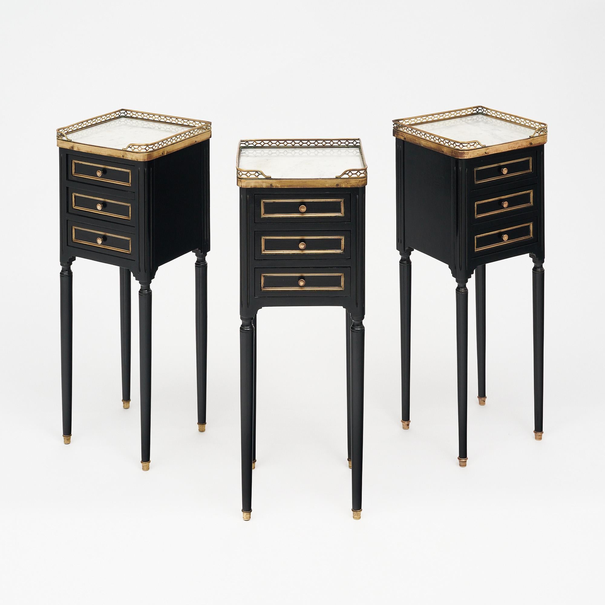 Set of three side tables in the Louis XVI style from France. This set is ebonized and finished with a lustrous French polish of museum quality. Each table has three dovetailed drawers and is topped with Carrara marble surrounded by a brass gallery.