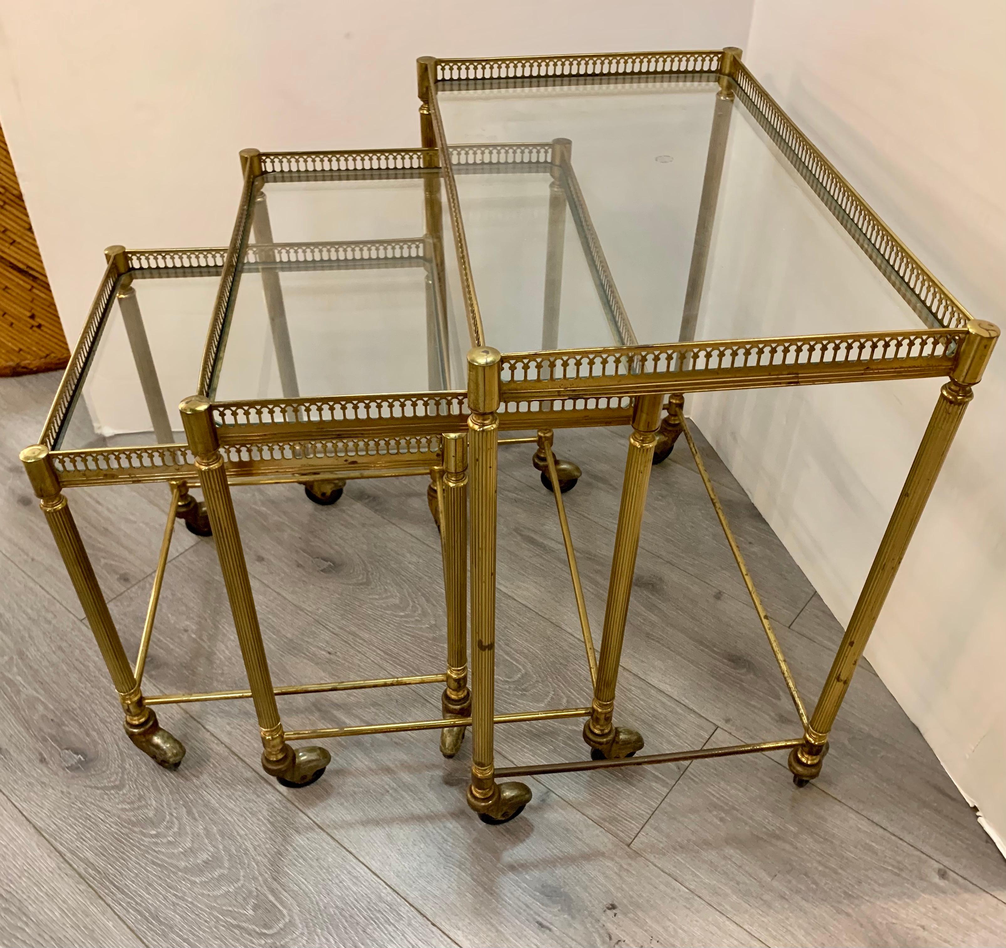 Set of three brass and glass top nesting tables with pierced brass galleries. All three on castors for ease of movement.