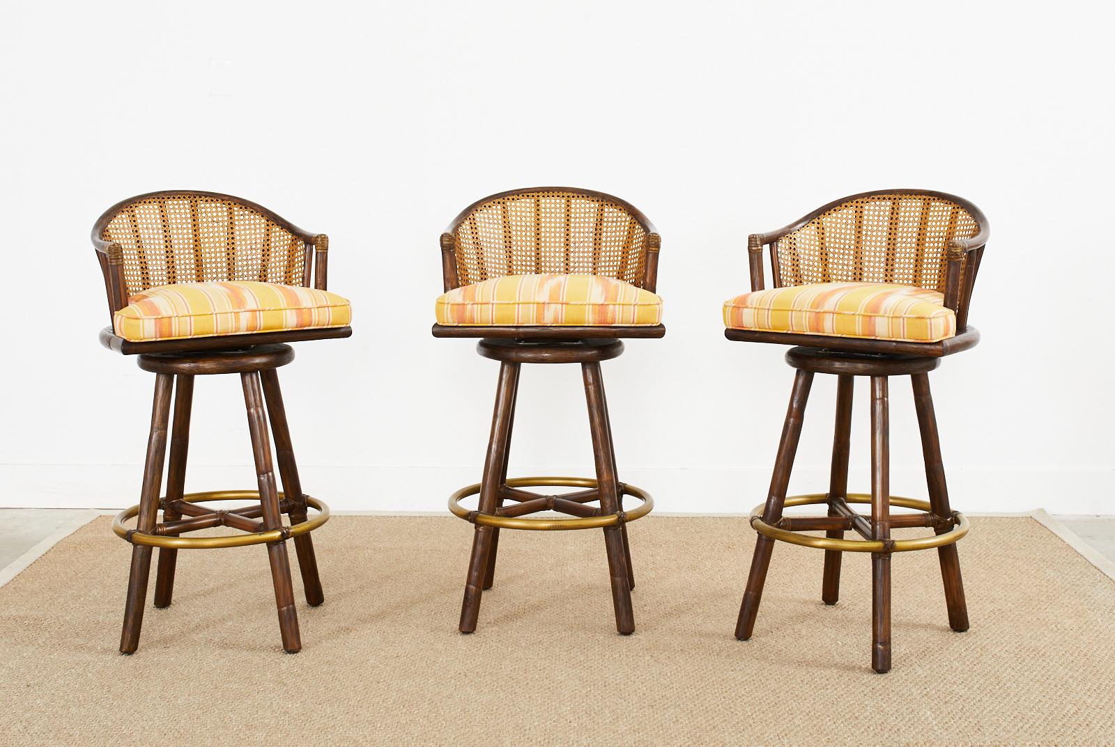 Fabulous genuine set of three organic modern style rattan barstools made by McGuire. The bar height stools feature a gracefully curved back with a cane inset. The swivel seats are upholstered with colorful striped fabric and mounted to a strong four