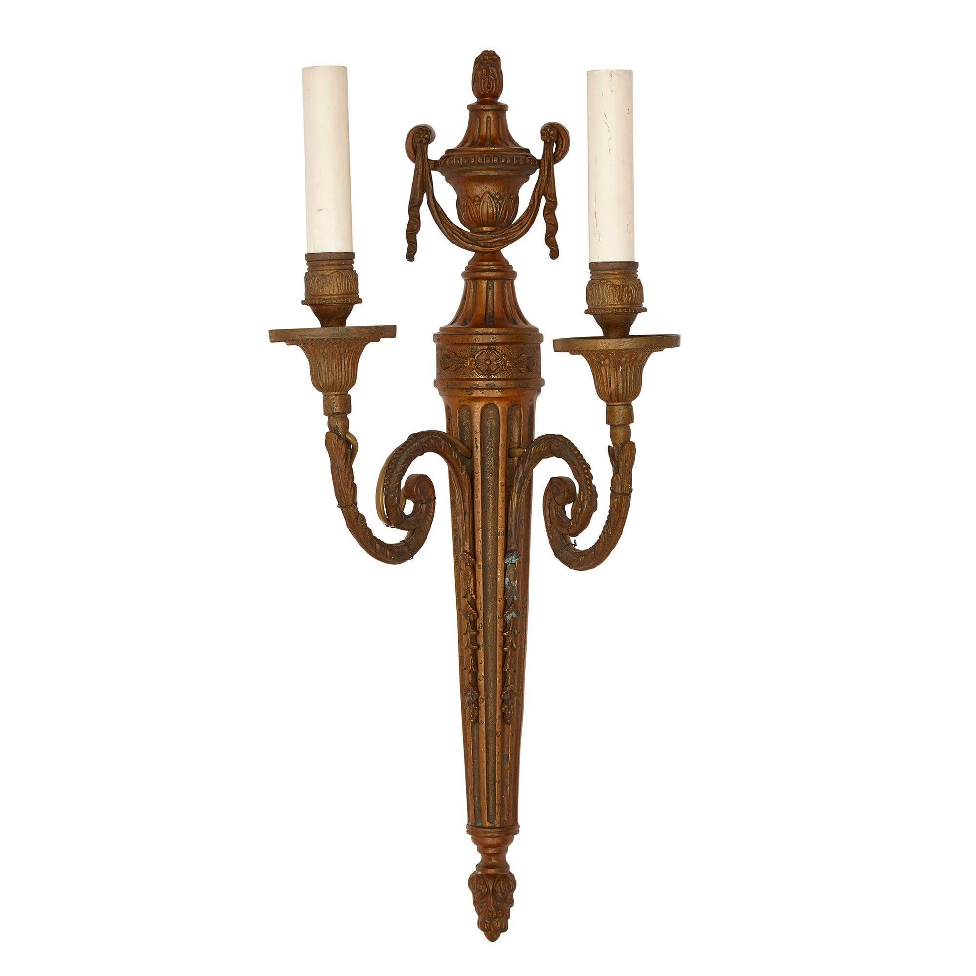 Set of three metal sconces in the neoclassical style
French, 20th Century
Height 52cm, width 23cm, depth 15cm

Each sconce in this set of three is crafted from warmly patinated metal in the Neoclassical style. Each sconce features a shaft-form