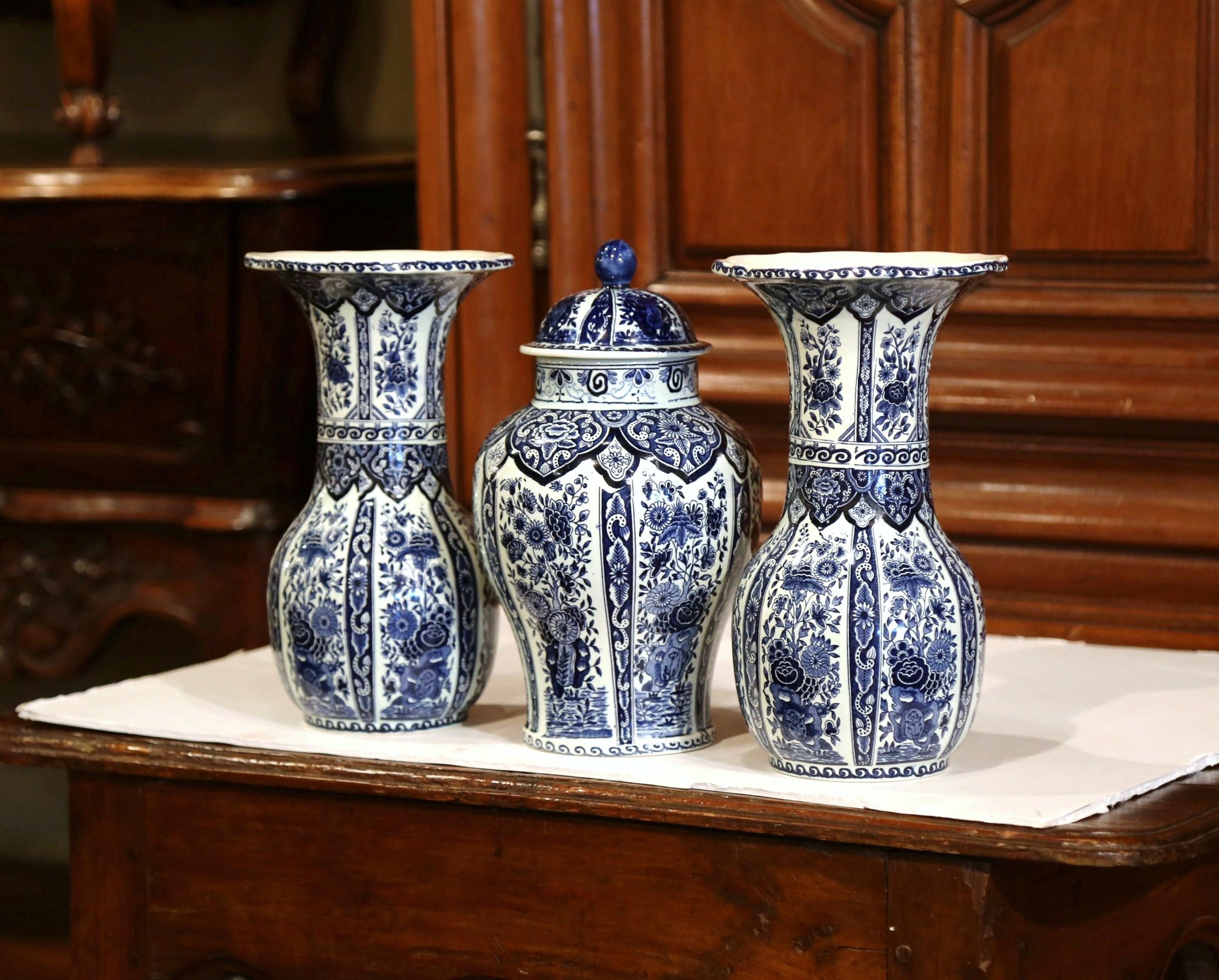 This vintage pair of ceramic Delft vases with matching ginger jar and lid was created in Holland, circa 1950. Round in shape the ceramic flower vases and the jar feature traditional hand-painted floral decorations. All pieces are stamped on the