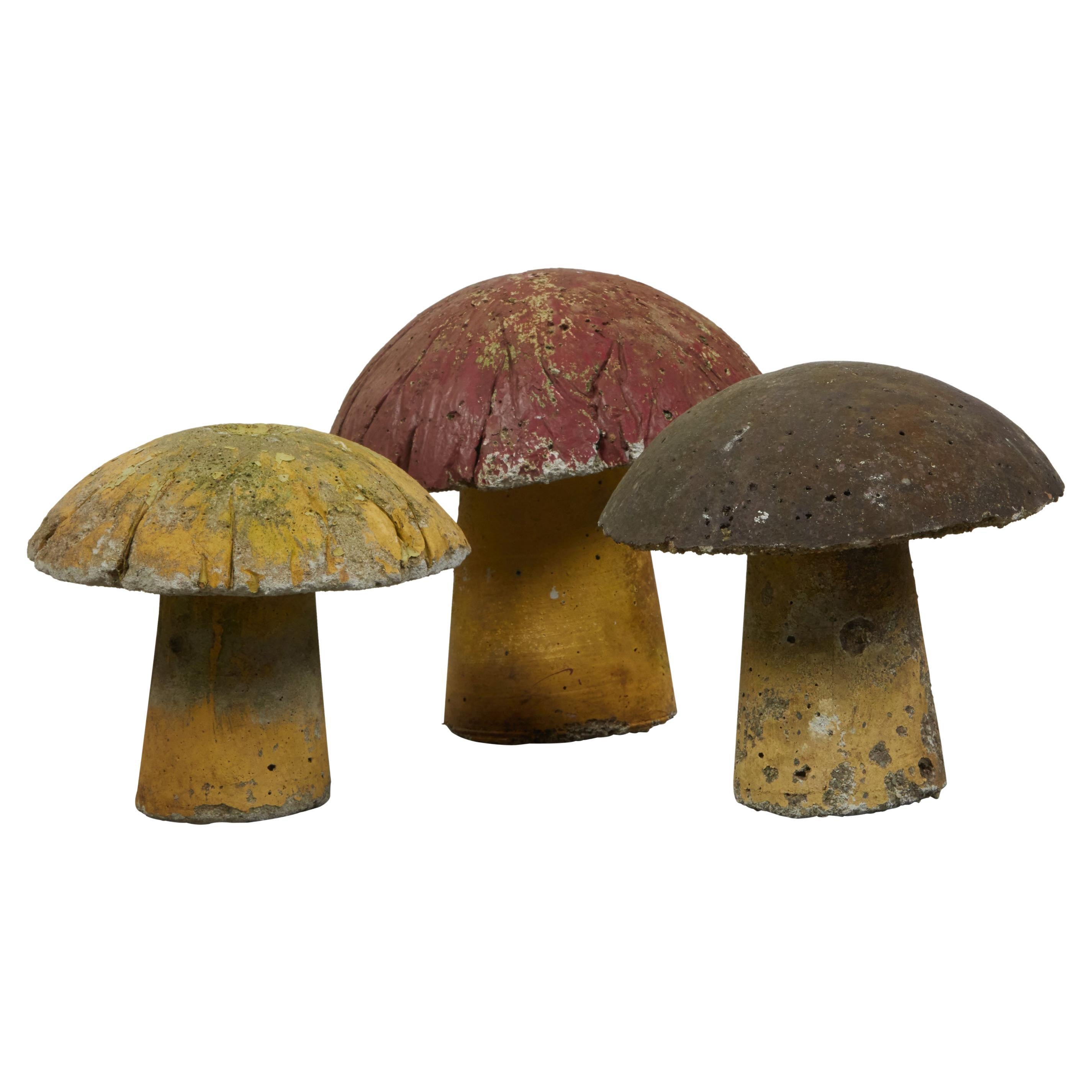 A set of three vintage American concrete mushrooms from the mid 20th century, with nicely worn patina. Made in the USA during the midcentury period, this set of three concrete mushrooms boasts a nicely weathered appearance with red, yellow and brown