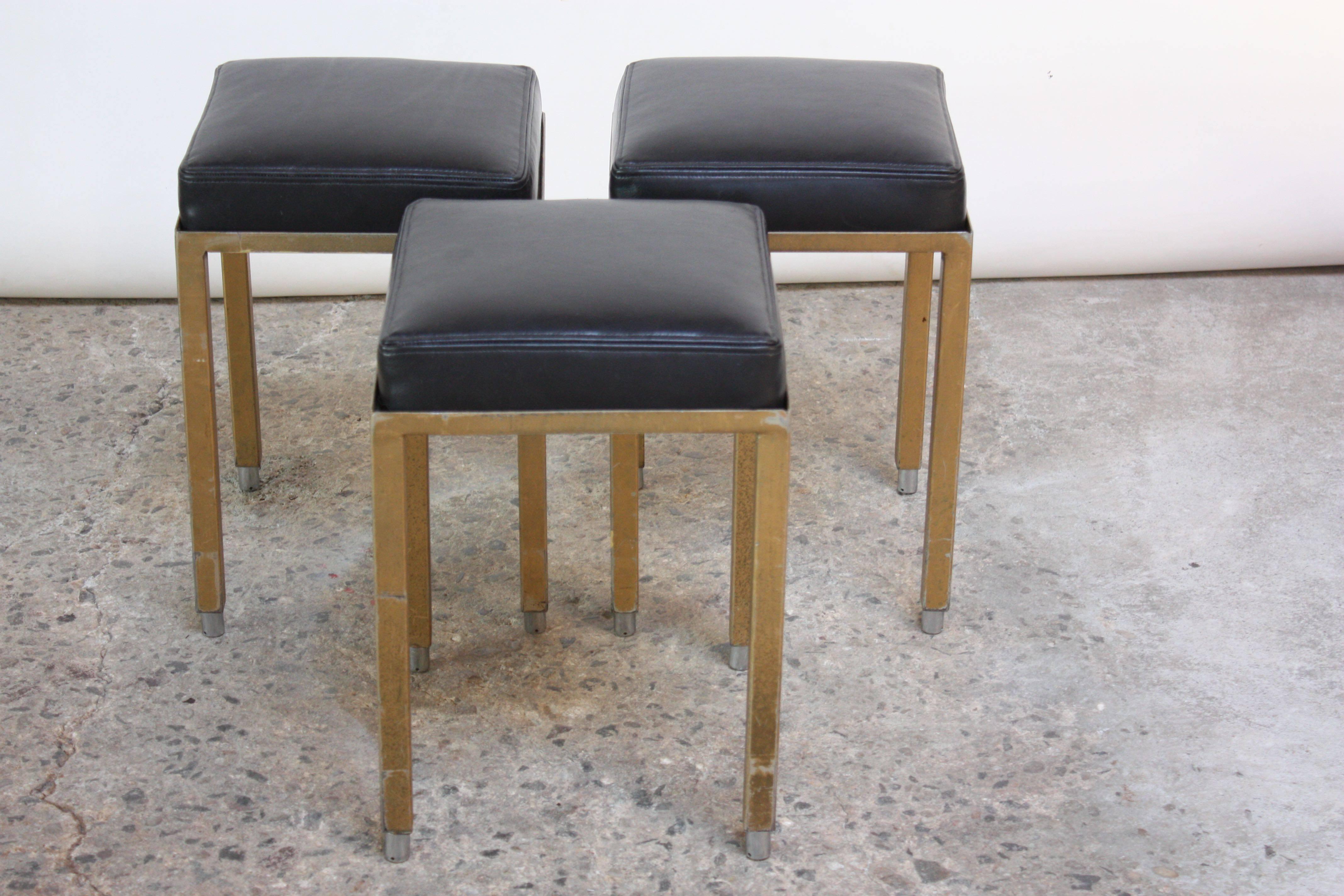 Set of three midcentury industrial low stools with leather cushions, painted steel bases and chromed-metal feet. 
Nice age, wear, and paint loss to the frames, but the double stitched black leather and foam are pristine and new. Stools can stack,