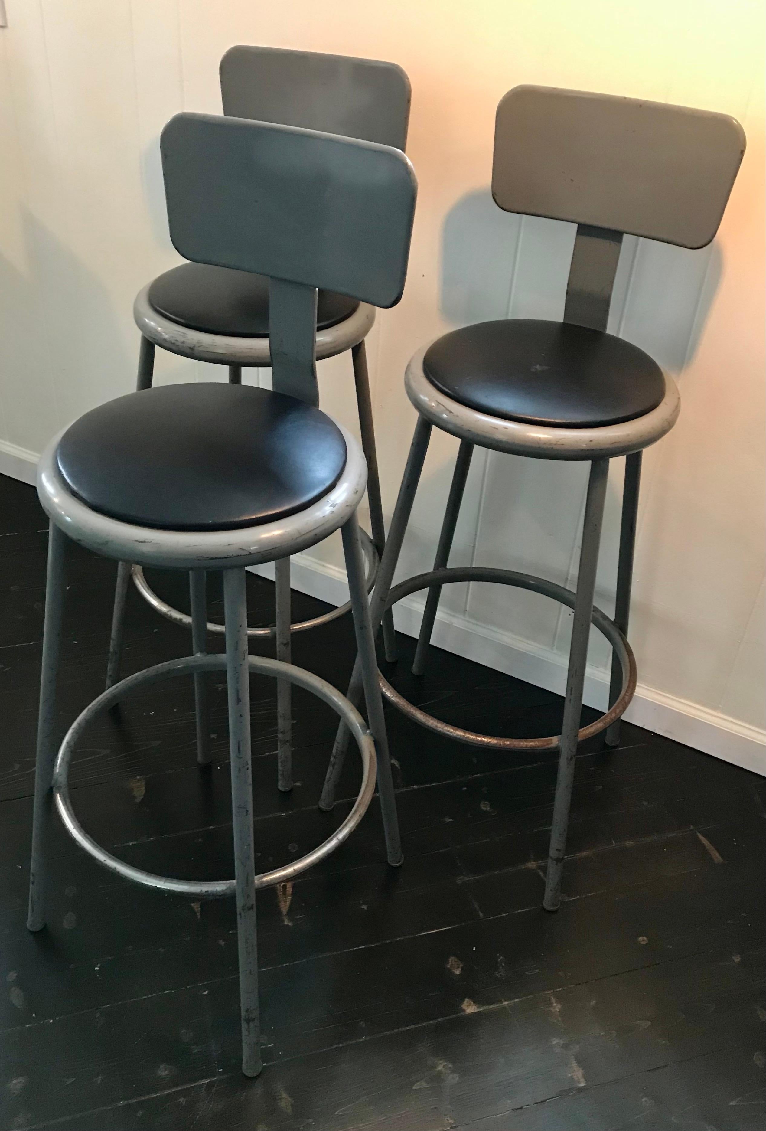 Authentic set of three Industrial bar height stools with back rests, round black vinyl seats. All original and very sturdy, wear appropriate with use, very cool. Made by Inter Royal Corporation, USA.
