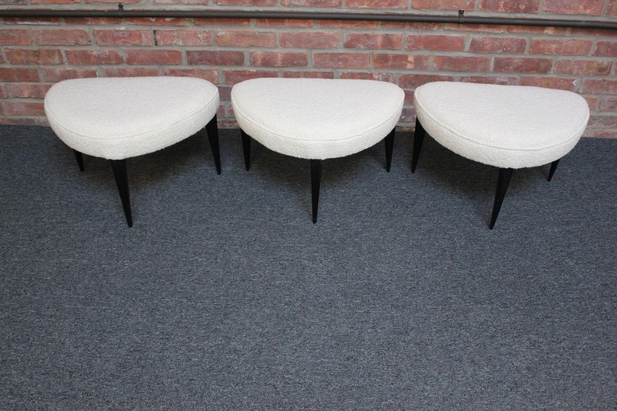 Set of three, half moon-form footstools/ottomans sourced in Rome, Italy newly upholstered in a cream bouclé (circa 1950s, Italy).
Sculpted ebonized legs (three per stool) boast sharp, dramatic lines, and the original black lacquer contrasts nicely