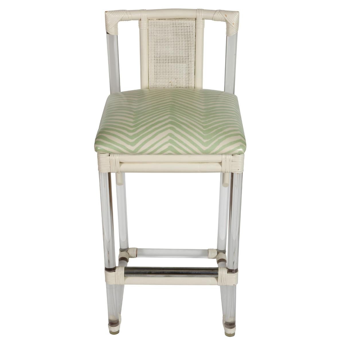 Ensemble élégant de trois tabourets de bar en lucite et rotin du milieu du siècle, nouvellement recouverts de tissu laminé Quadrille. Avec ses cadres en lucite élégants, ses détails en rotin peint en blanc et sa canne centrale, cet ensemble allie le