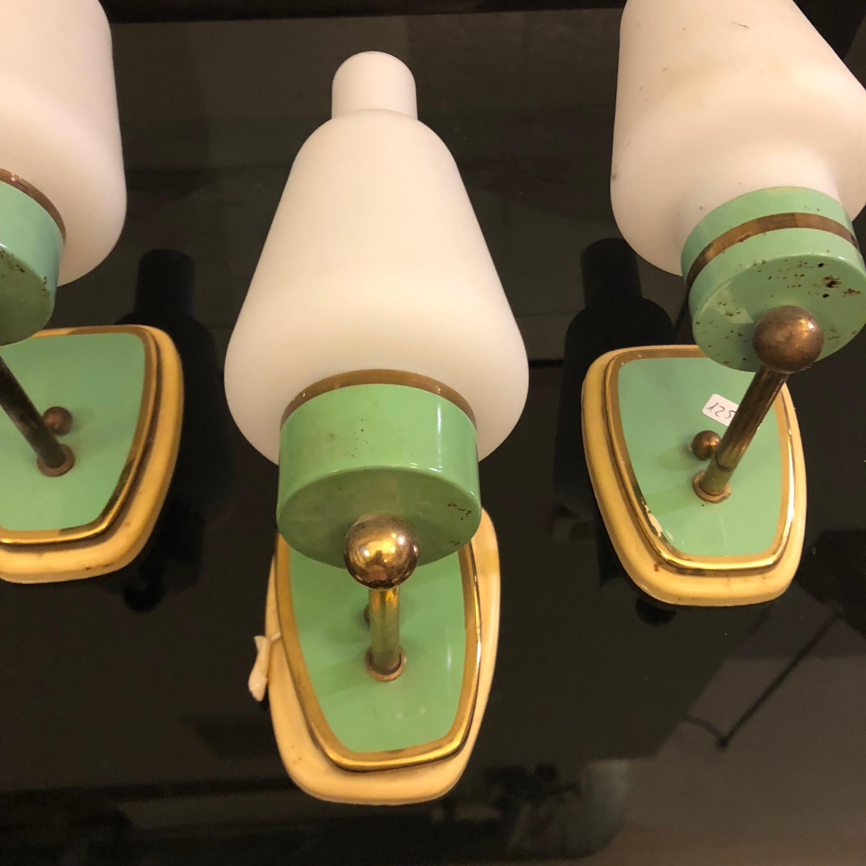 Three green painted brass and white glass wall sconces. Ivory plastic base, they work with 110-240 volts and regular e14 bulbs.