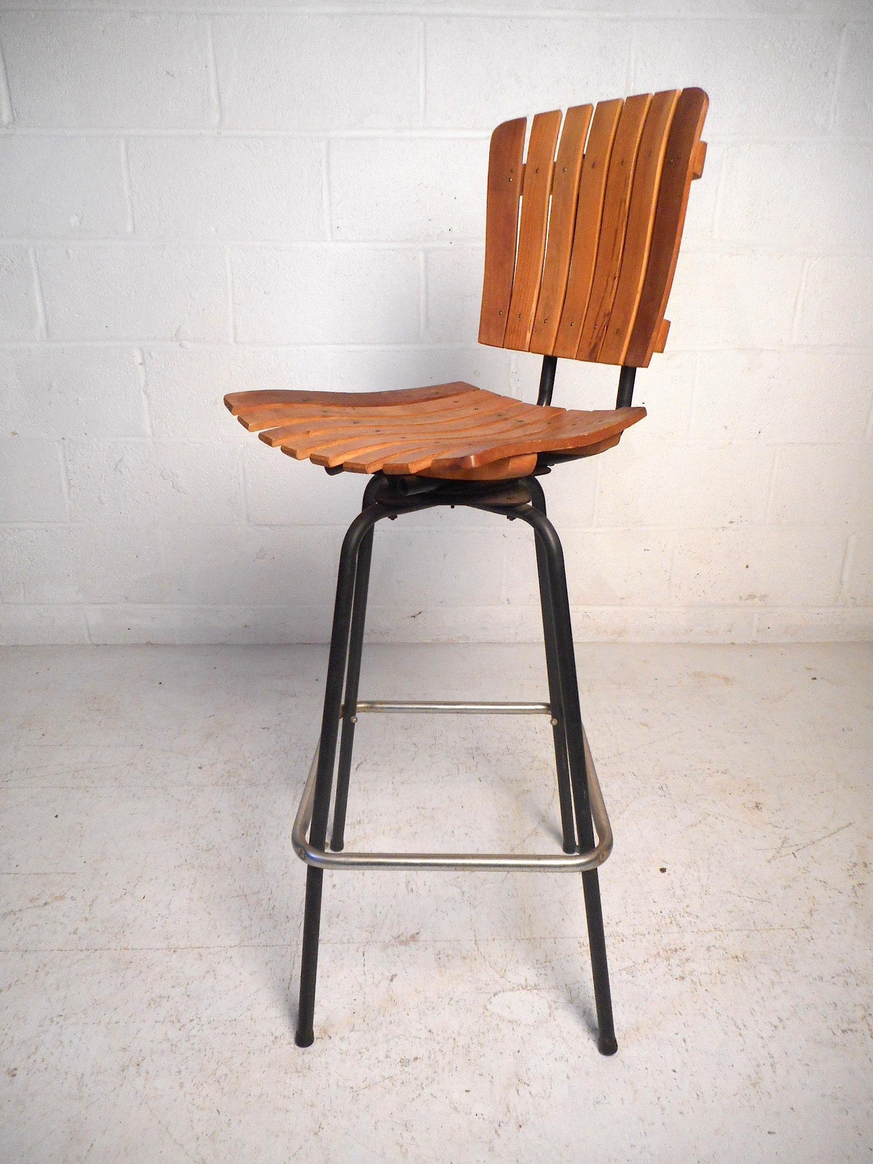 This stylish set of midcentury bar stools feature slatted wooden seats and backrests, sturdy iron frames with steel footrests, and swiveling bases offering a dynamic seating solution. In the style of Arthur Umanoff, these stools are sure to make an