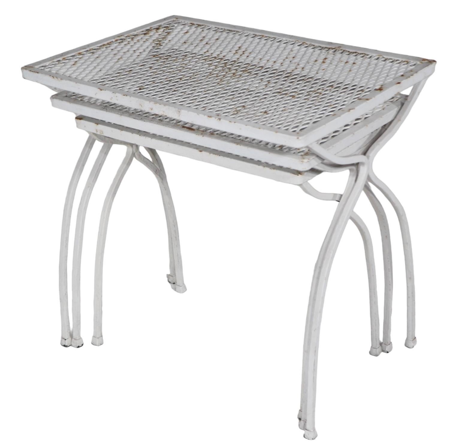 Classic Mid Century wrought iron and metal mesh garden, patio, poolside nesting tables attributed to Salterini, circa 1950's. The tables feature  stylized legs of squared iron, with rectangular metal mesh tops, perfect for either indoor or outdoor